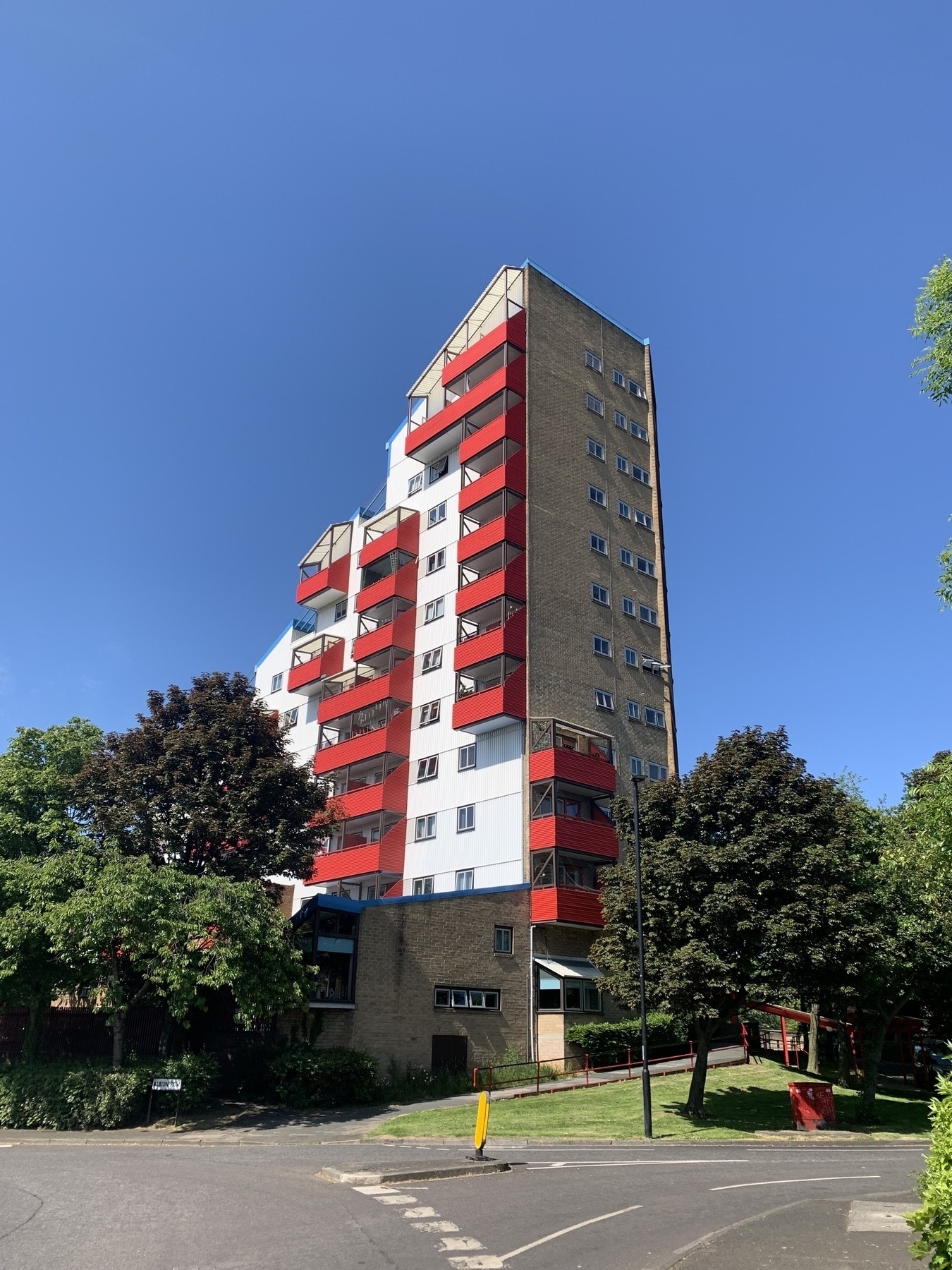 Tower block with white cladding and red balconies set against a bright blue sky