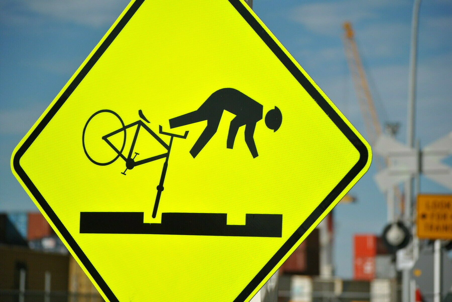 Diamond shaped yellow roadsign in focus with a person going over the handlebars of a bike that has it's wheel caught in a railway track.