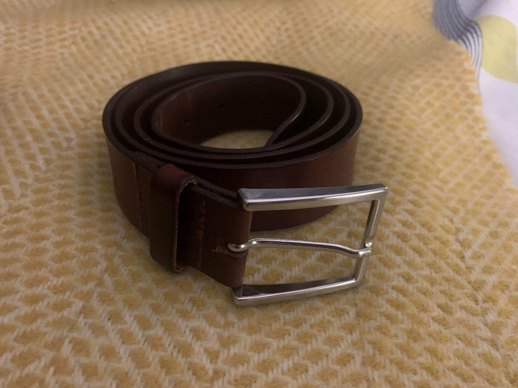 Coiled brown leather belt with silver buckle on top of yellow wool quilt.