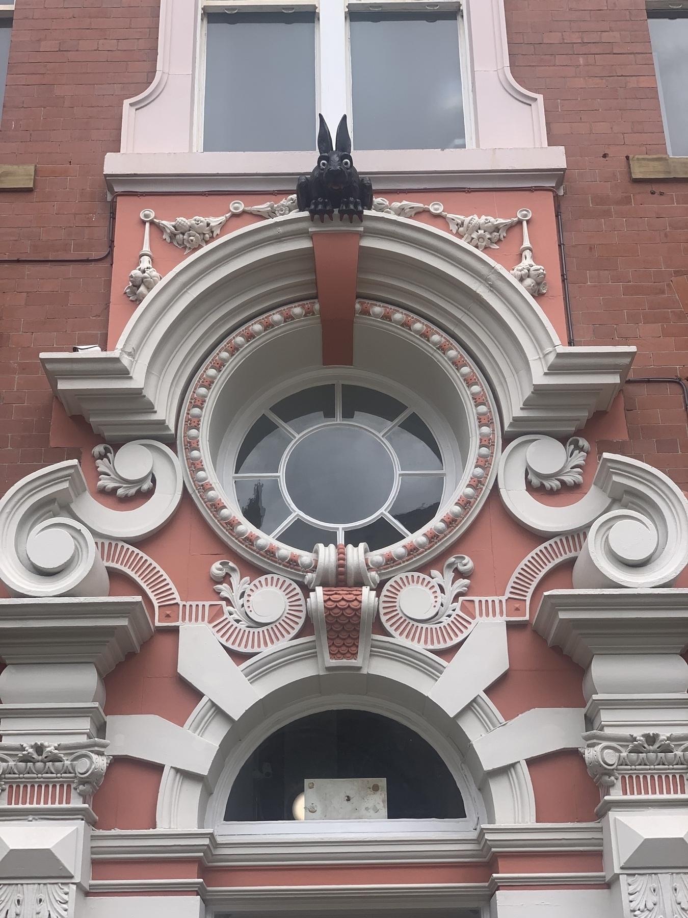 Decorative white and pink doorway with black vampire rabbit gargoyle perched above a circular window.