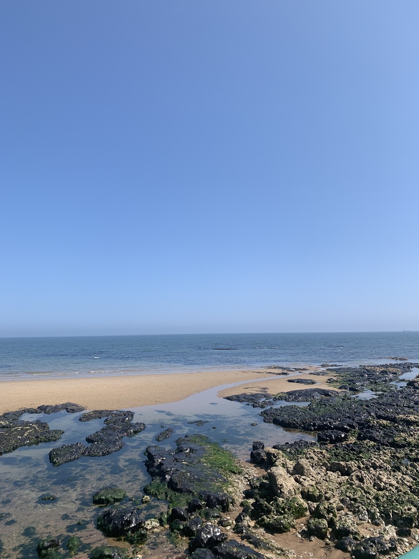 Looking out to sea over sand and rock pools. Dark blue sea blends into a bright blue sky on a sunny day.