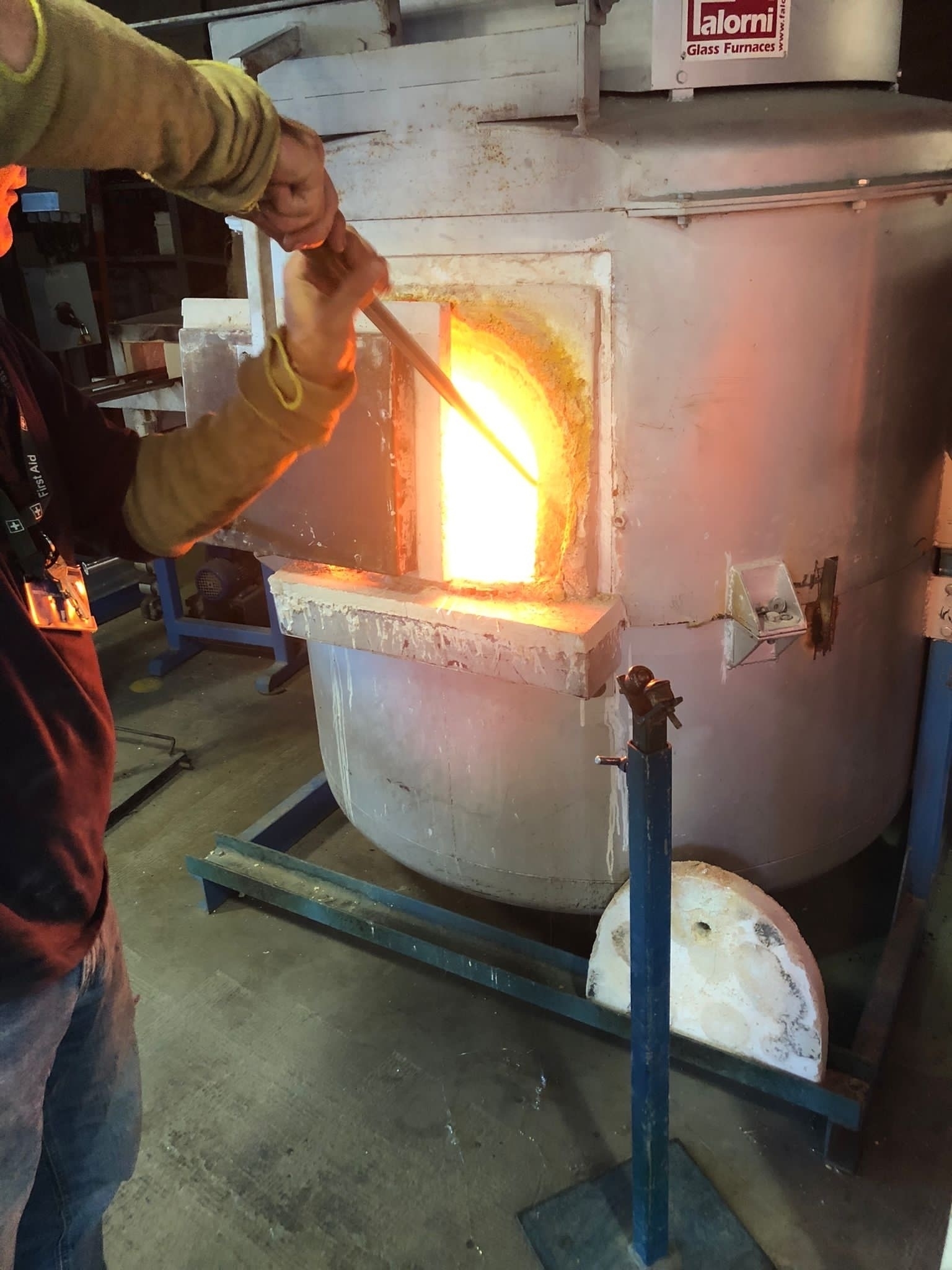 Metal furnace with door partially open and person holding a rod in the glowing heat.