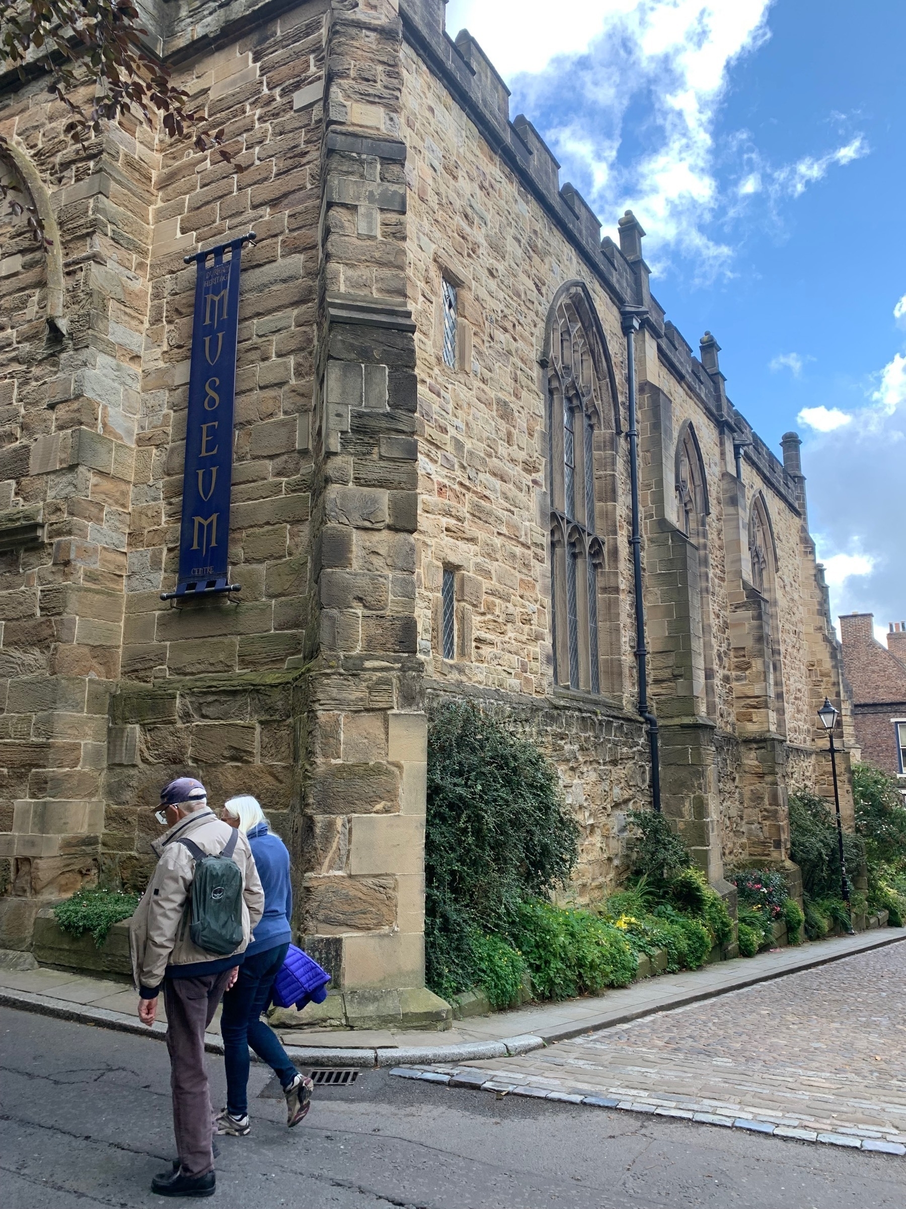 Two people walking in the road in front of an old church building now a museum.