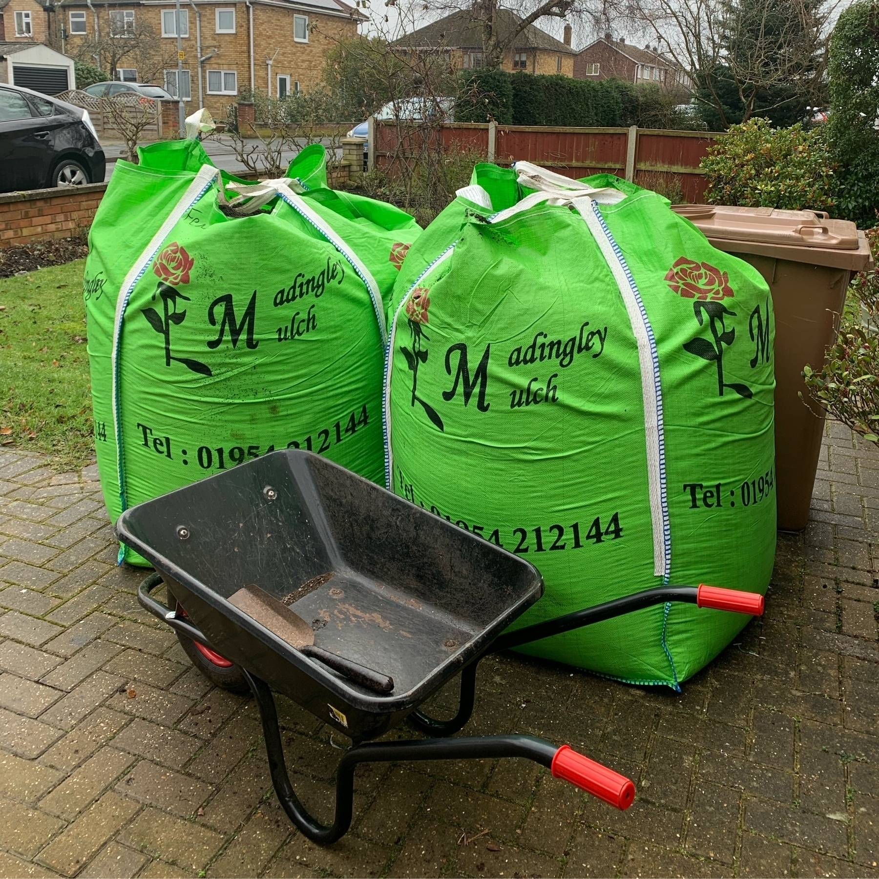 Two huge green bags full of soil. A wheelbarrow in the foreground