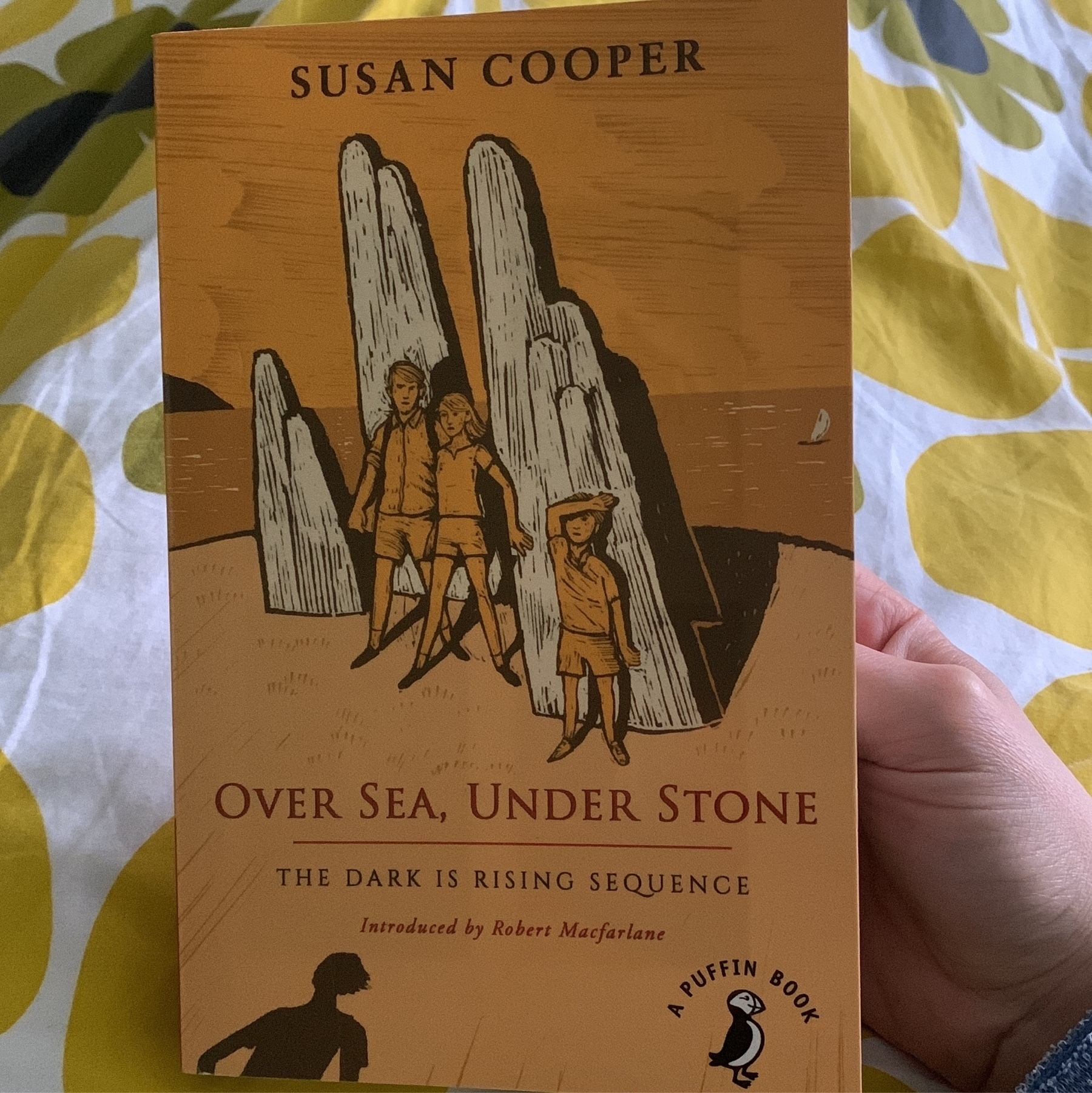 Book cover of Over Sea, Under Stone by Susan Cooper. Background is a duvet cover with bold yellow flower design.