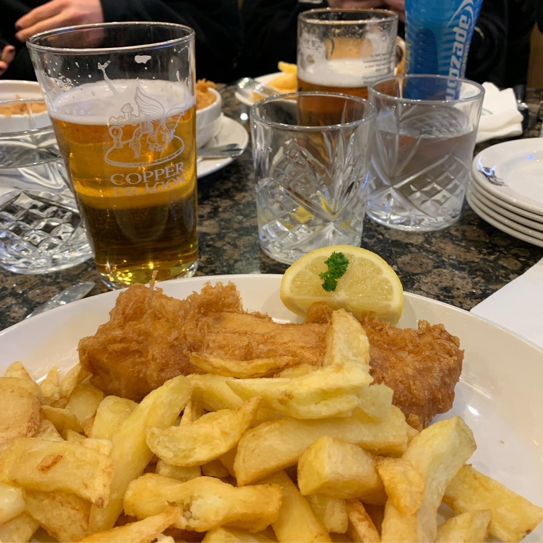 Plate of fish and chips in foreground with pint of beer behind
