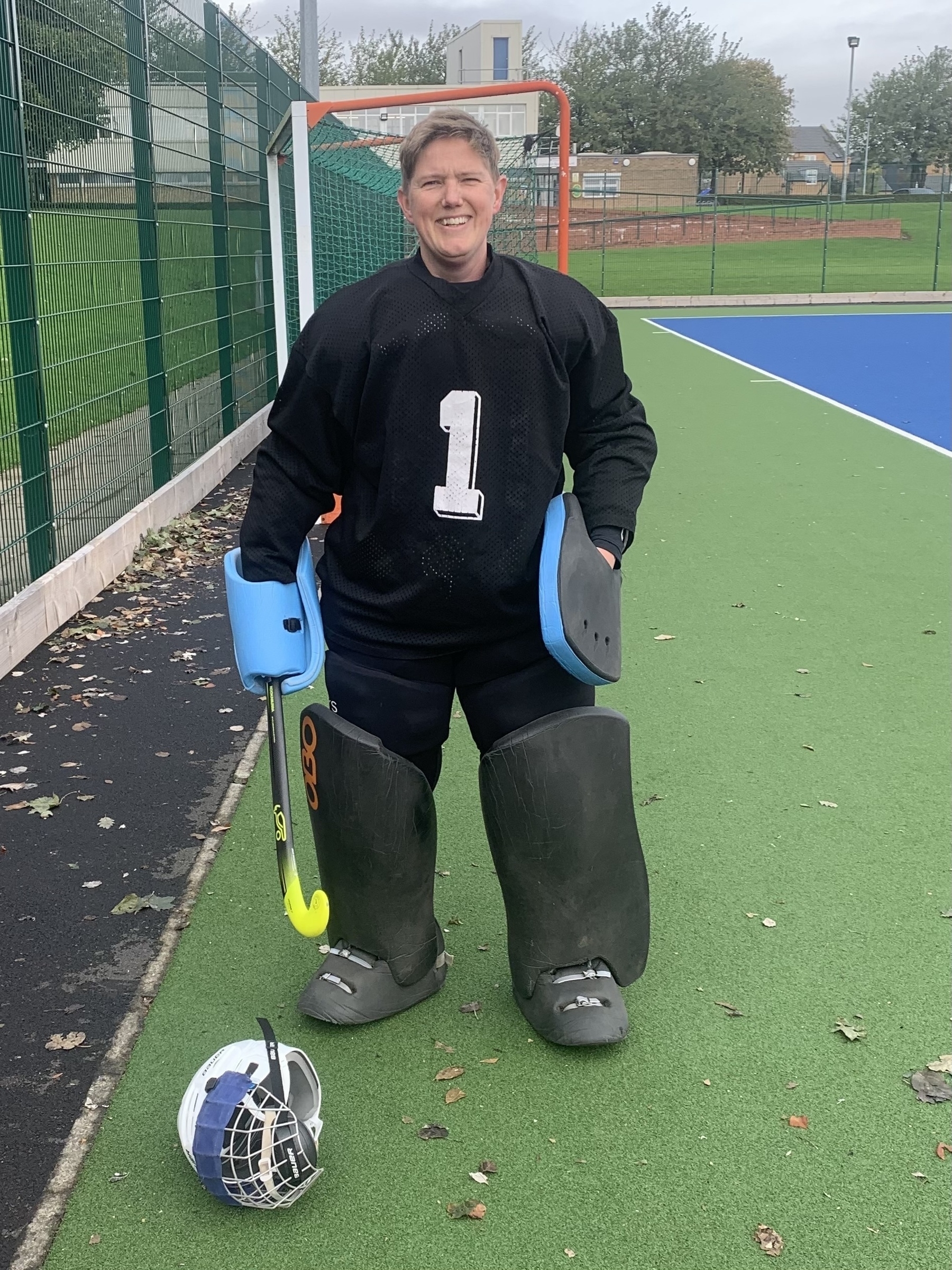 Fully kitted up field hockey goalkeeper minus helmet which lies on the pitch before them.