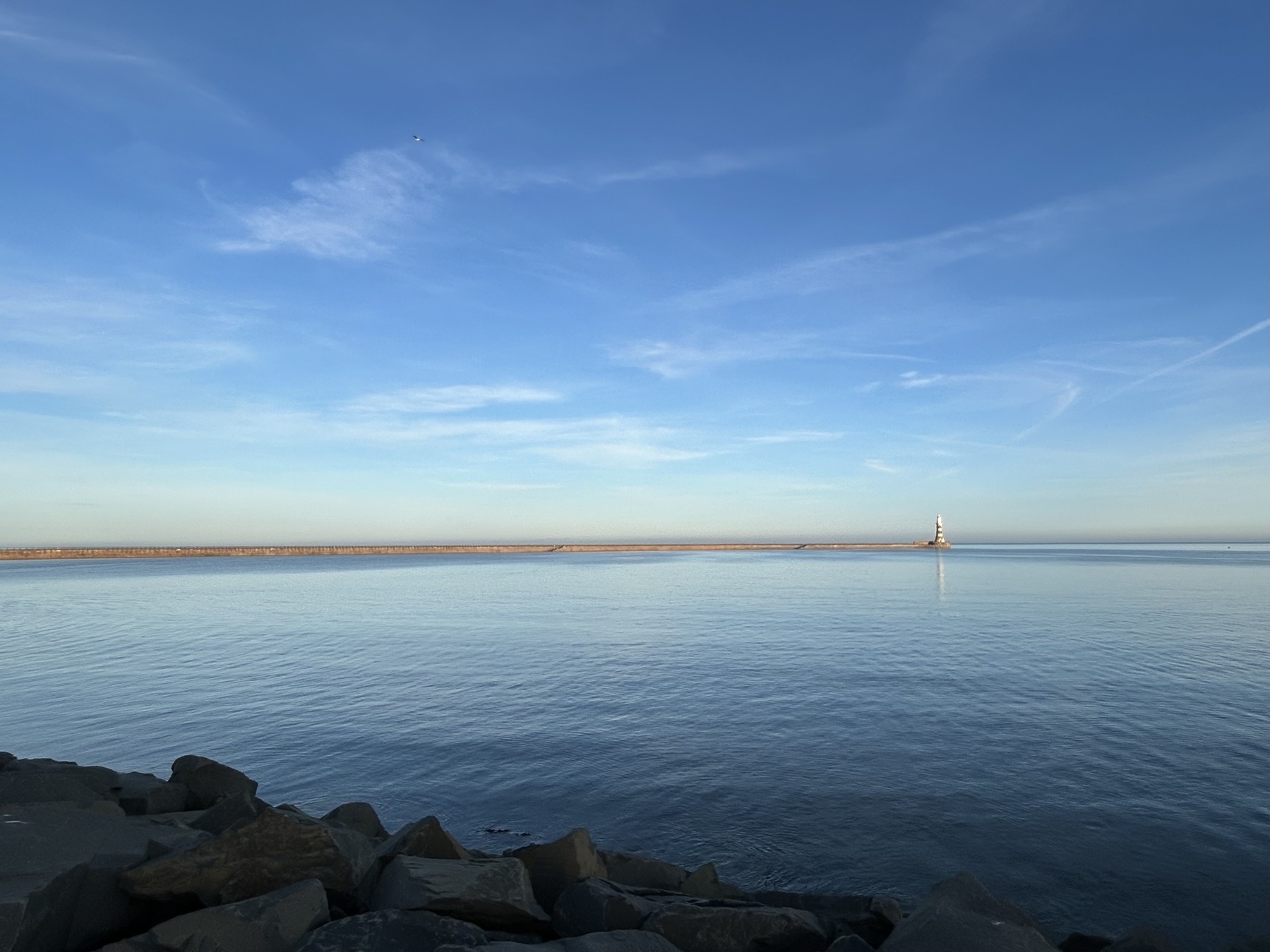 Lighthouse in the distance against a calm sea and bright blue sky.