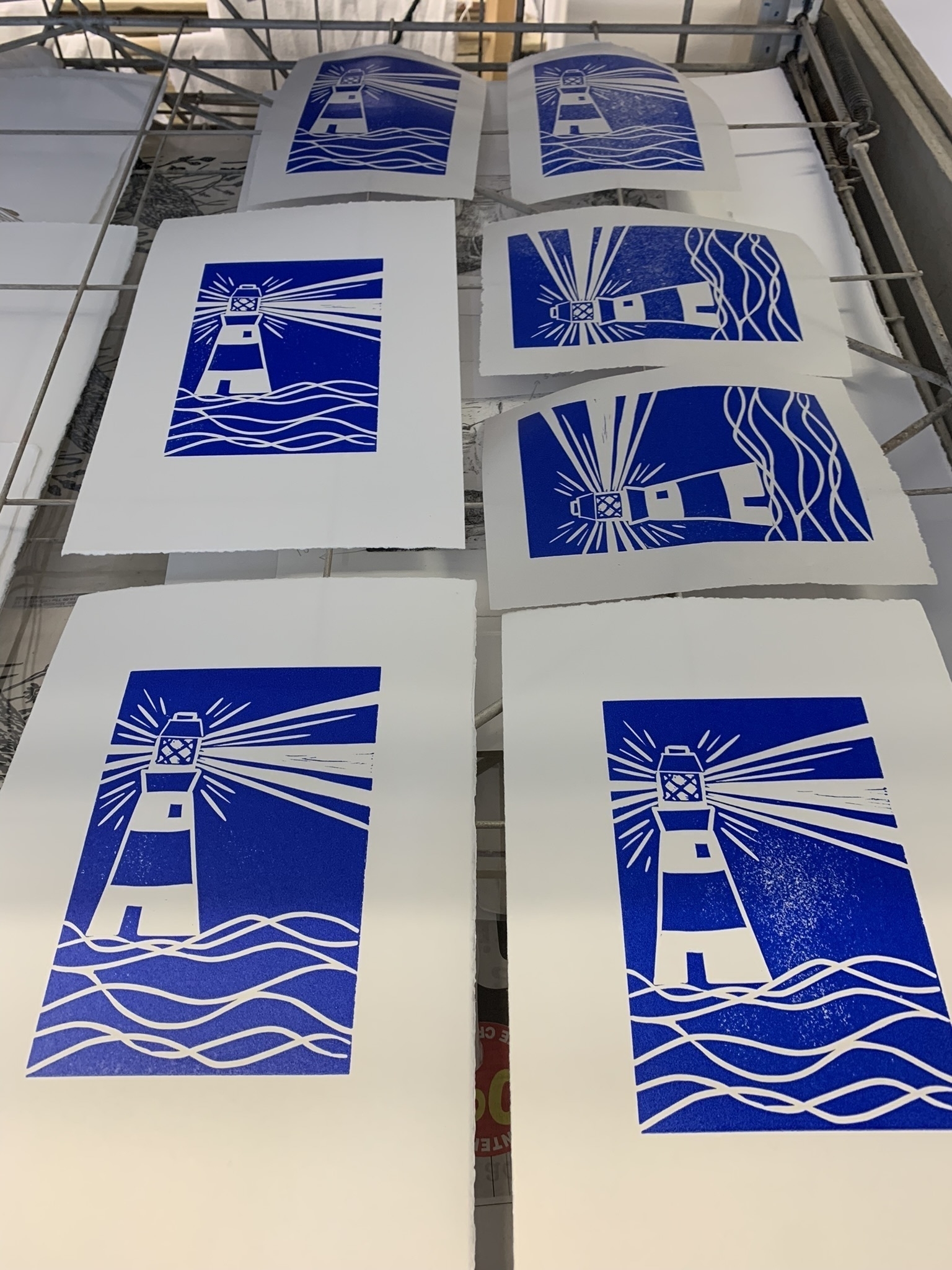 Lino cut prints of a simple lighthouse design in brilliant blue resting on the drying rack.