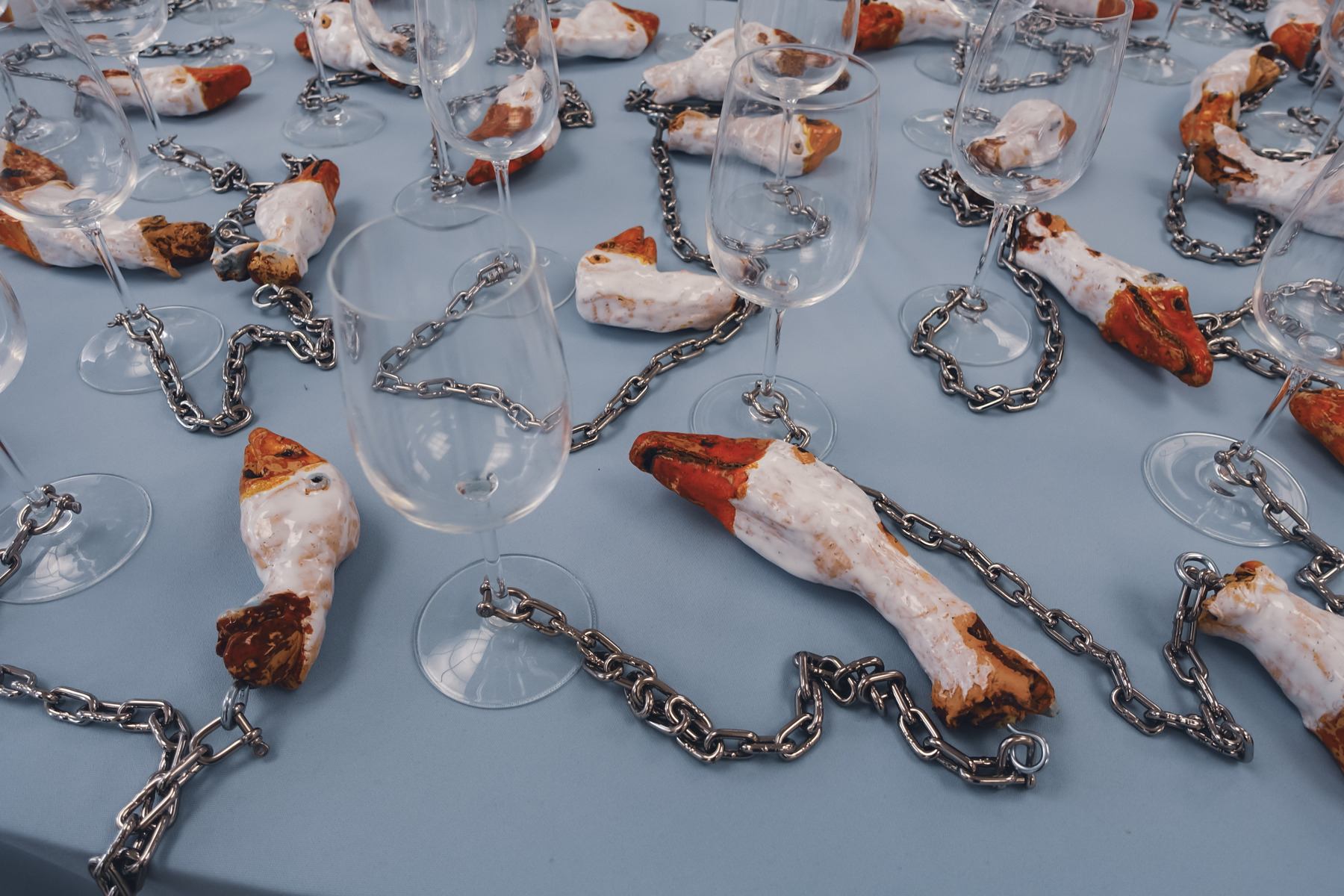 Ganzenhoofden van porcelein (?) die afgehakt lijken en aan kopjes vasthangen op een tafel met blauw tafelkleed door Ignace Cami