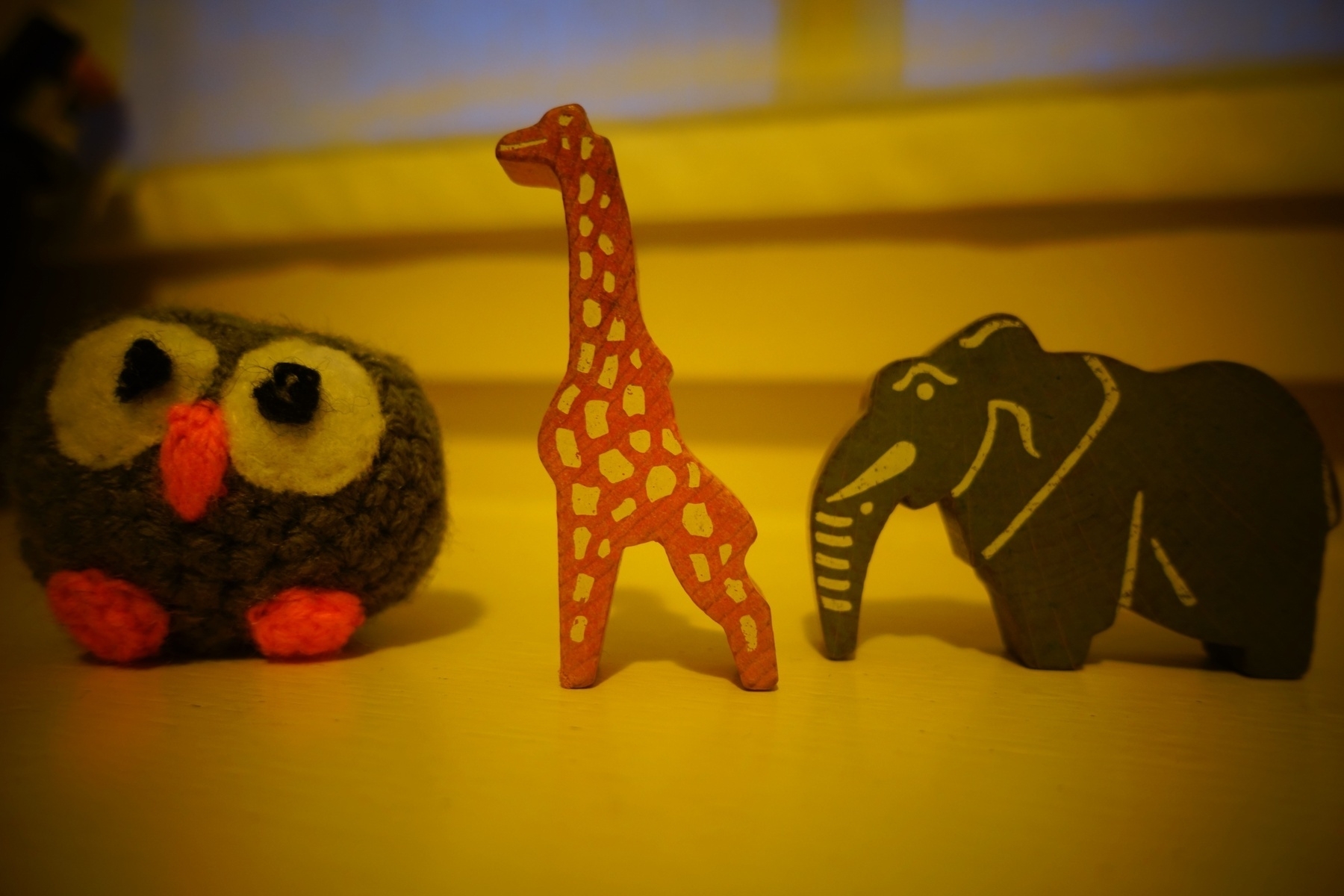 An owl in wool, a wooden giraf and a wooden elephant with a warm yellow filter as camera effect