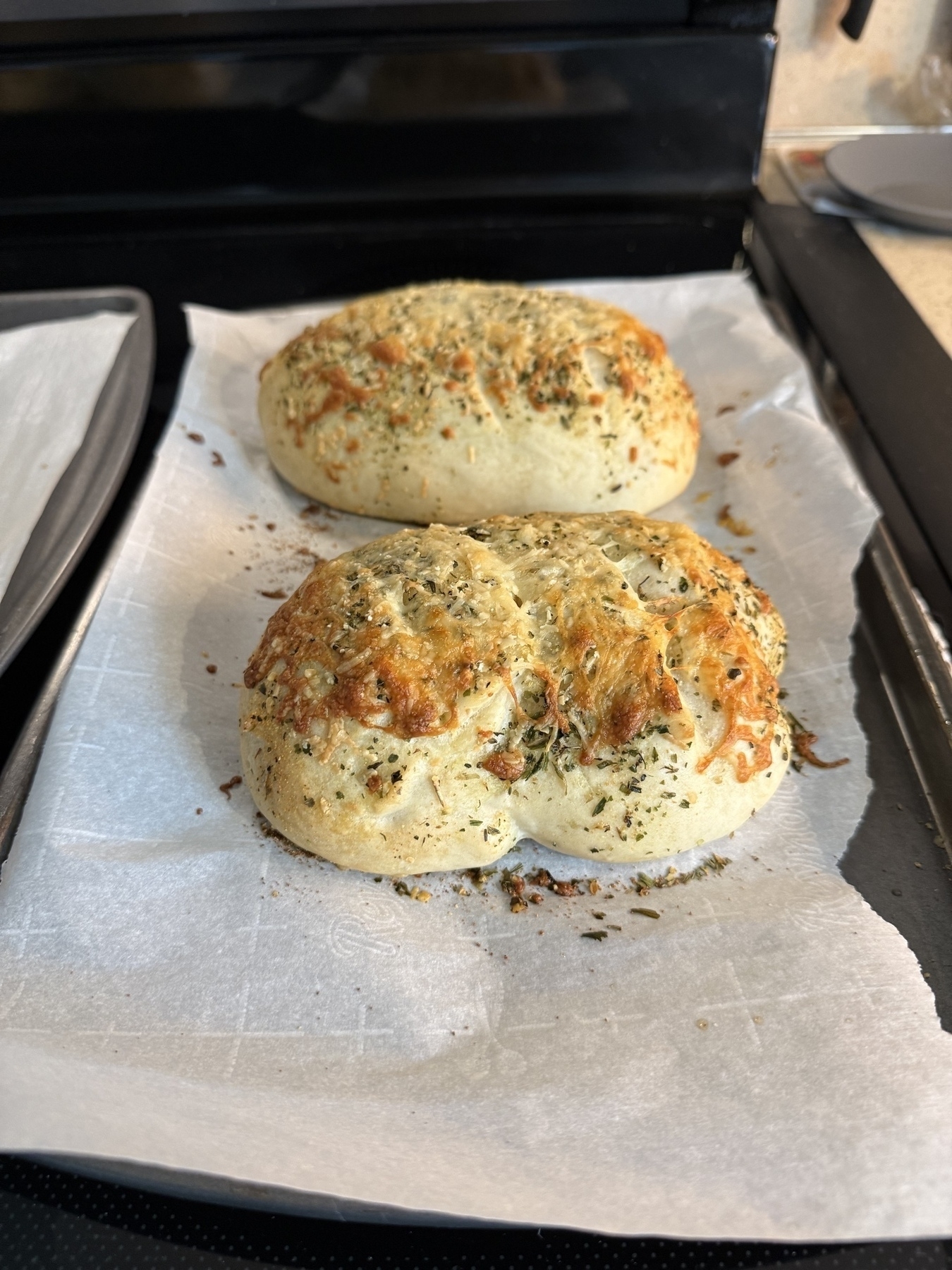 Two freshly baked loaves of bread on a baking tray, browned cheese crusty on top