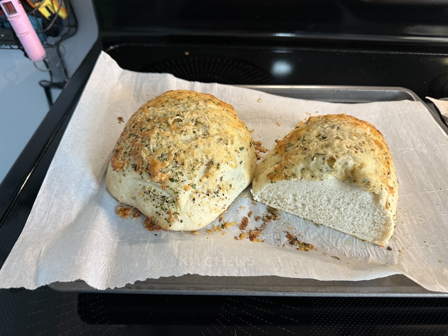 Two freshly baked loaves of bread on a baking tray, one sliced open to show a nice white bread texture