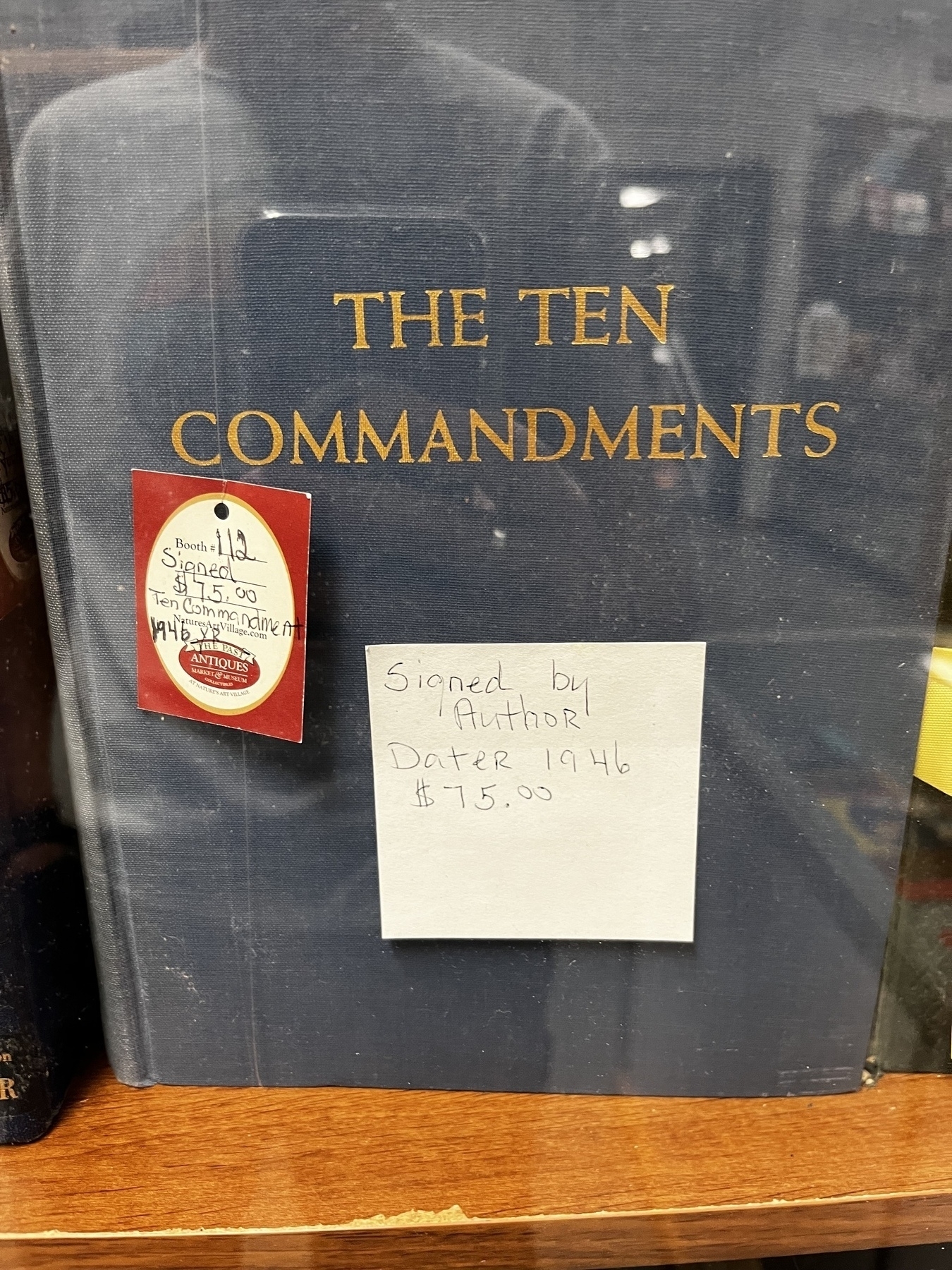 A large book titled The Ten Commandments with a post it note saying it is Signed By Author and a price tag of $75