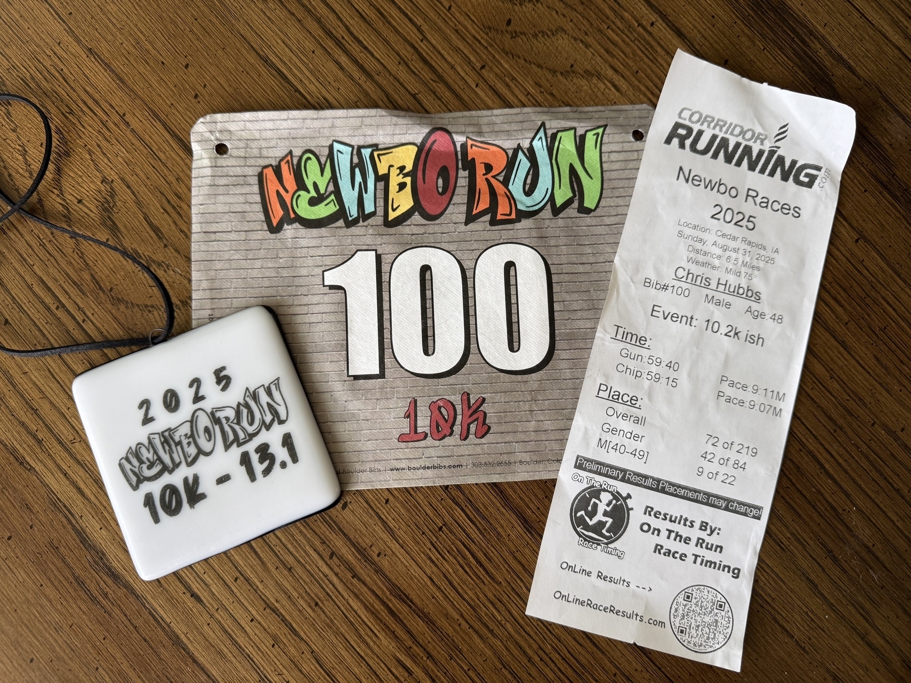 Picture of a race bib that says “NewBo Run 10K”, a finishes medal, and a race timing printout saying Chris finished the 10.2-ish race with a 59:15 chip time.