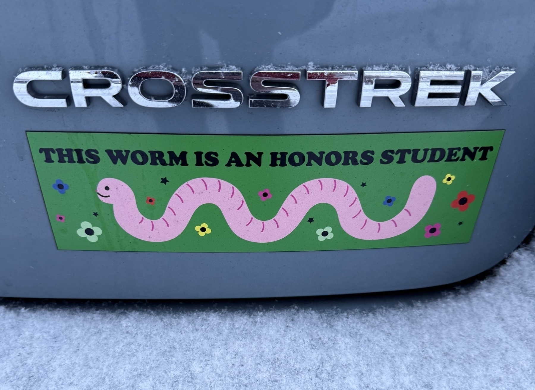 A bumper sticker below a Subaru Crosstrek logo showing a happy earthworm with the phrase “this worm is an honors student”.