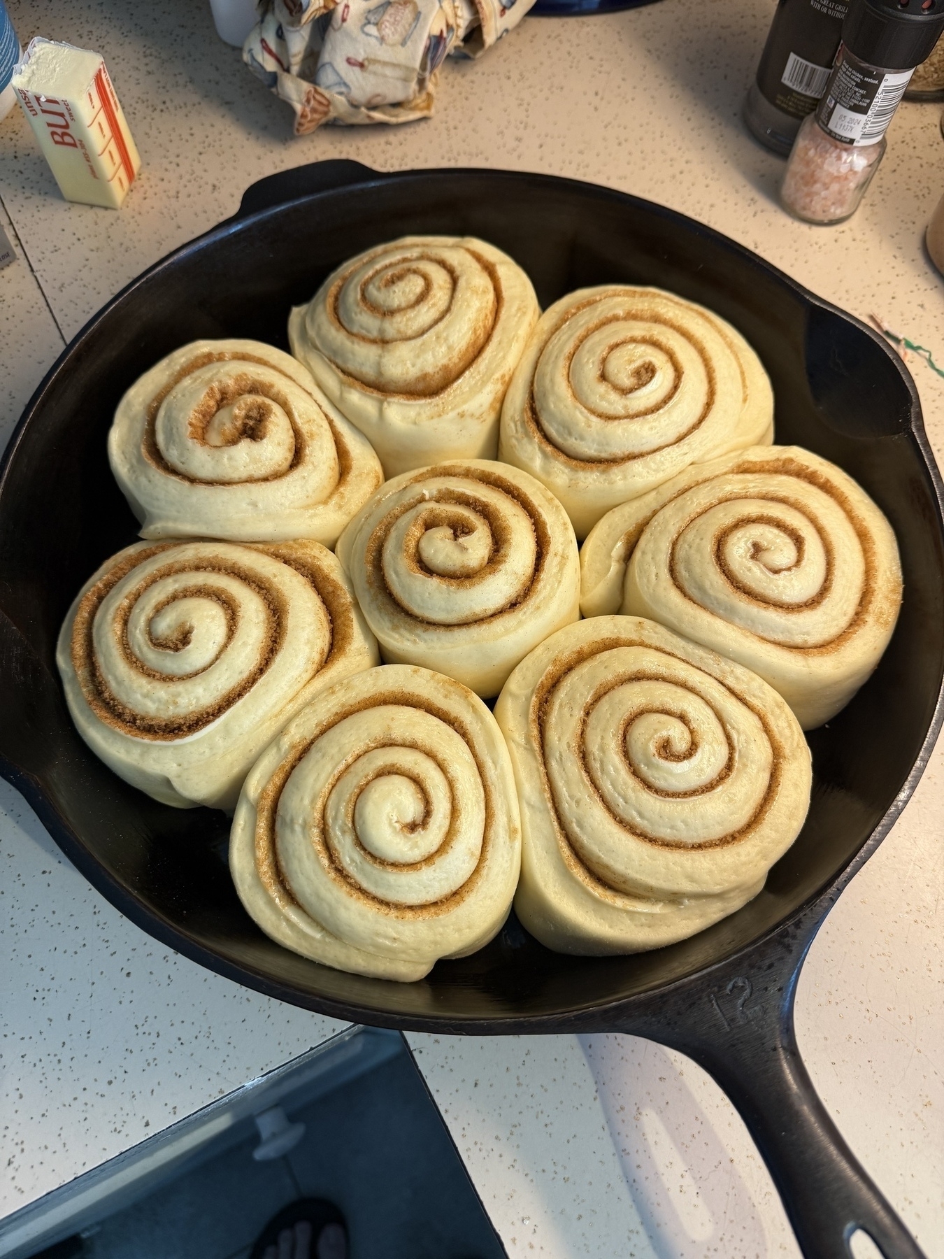 A large cast iron skillet filled with raised but unbaked cinnamon rolls