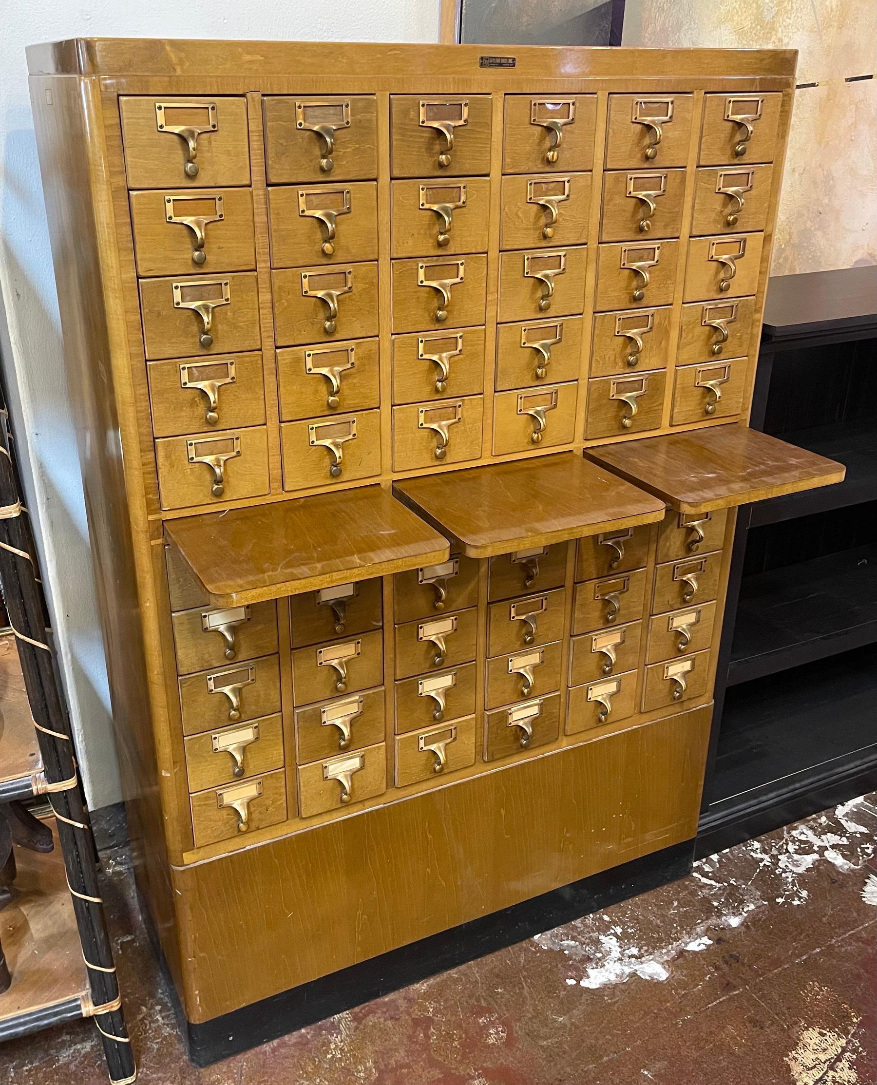A wooden card catalog cabinet with multiple small drawers and three fold-out writing surfaces is shown.