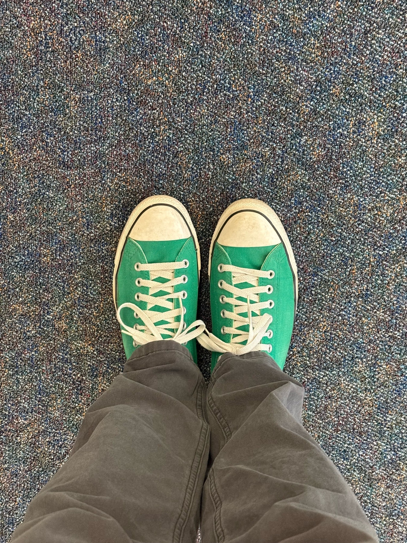 A pair of green converse shoes on a carpet floor