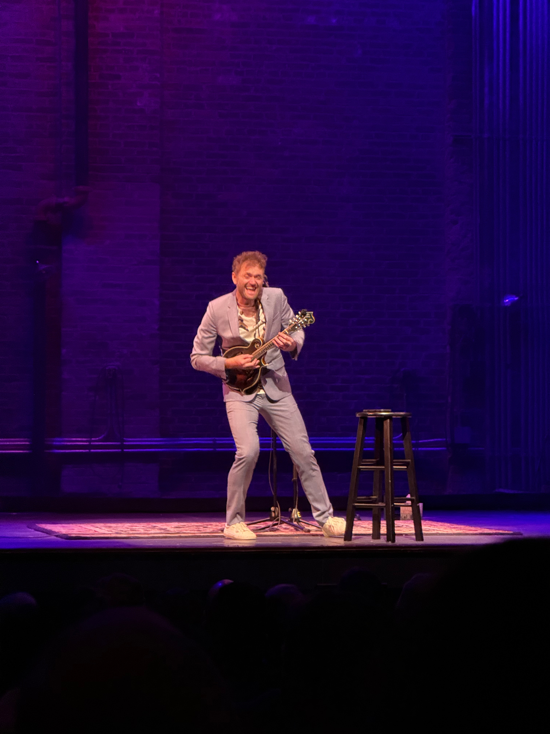 A man in a light suit on stage playing a mandolin