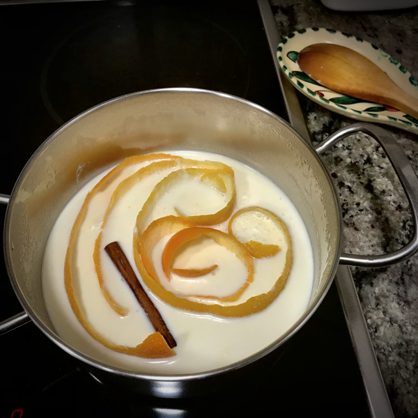 Cazo de leche calentando e infusionando peladura de naranja y de limón con una rama de canela. 