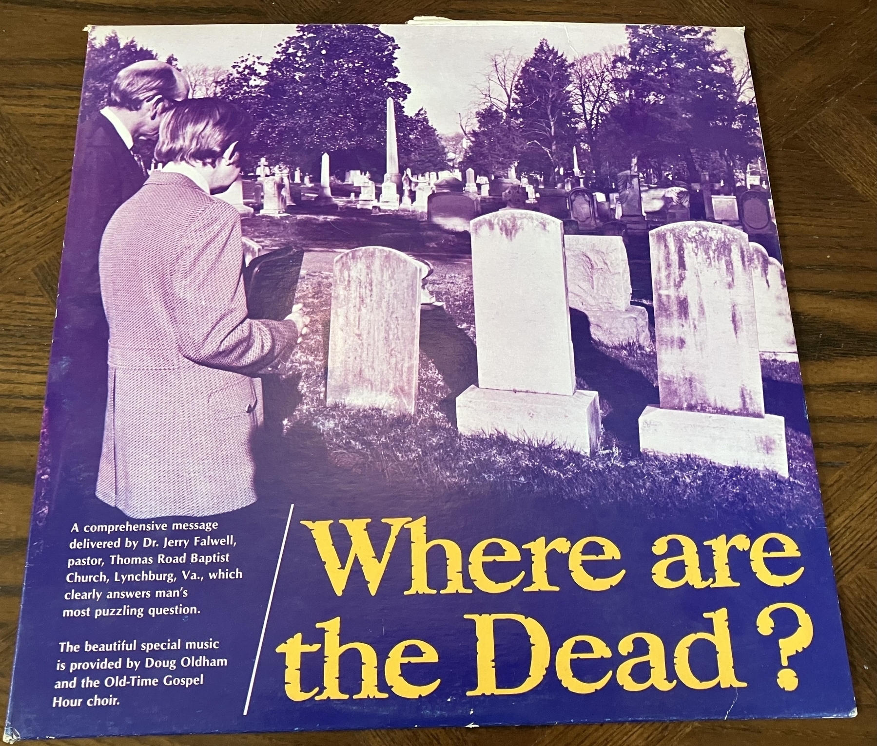 Purple tinged photograph of two men standing before a row of grave stones, with the album title “where are the dead?”