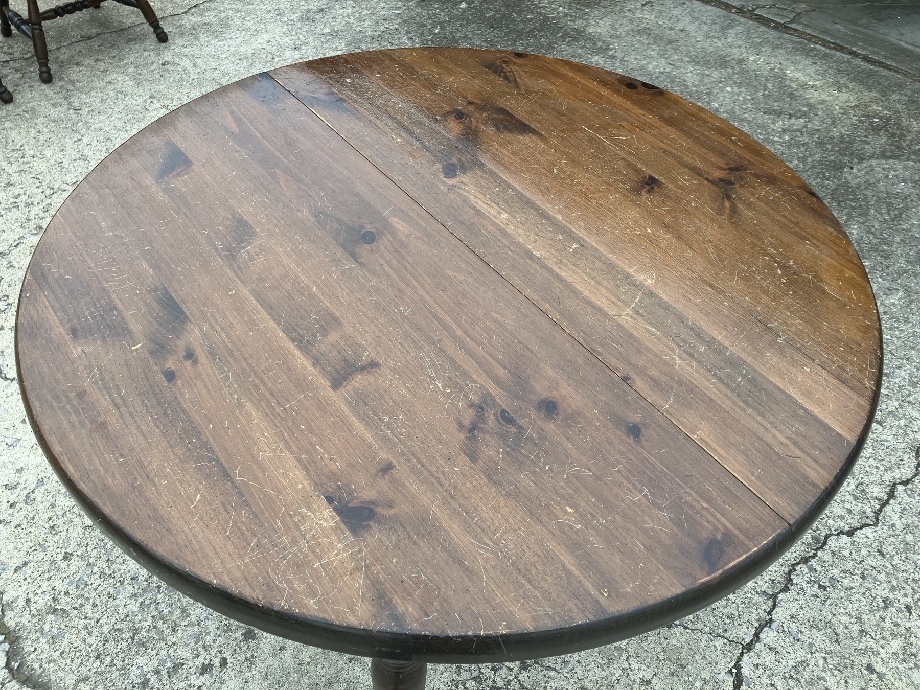 Auto-generated description: A round, wooden table with a slightly worn surface is set on a concrete floor.