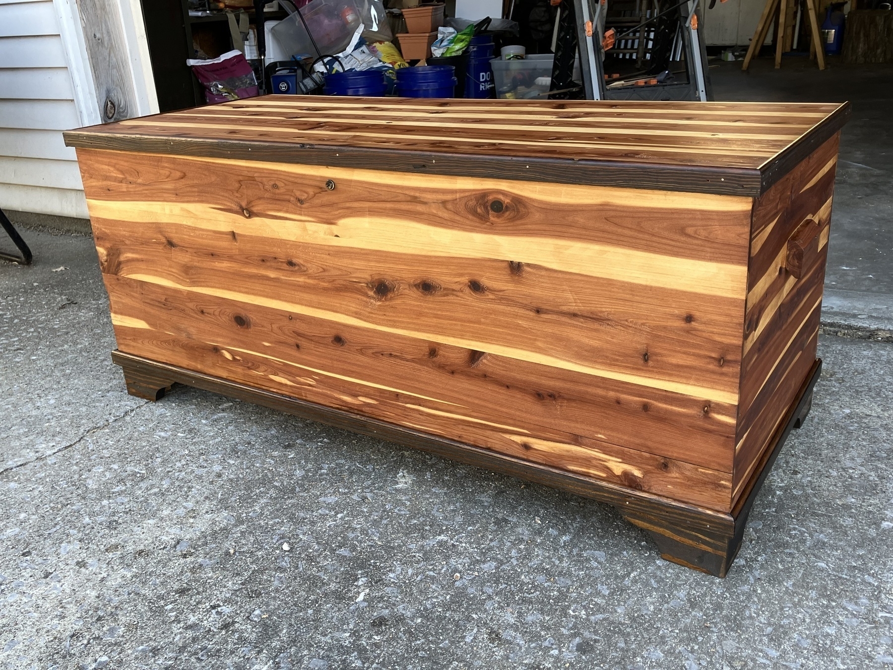 Auto-generated description: A wooden chest with a multi-toned wood grain design is placed on a concrete floor in a garage.