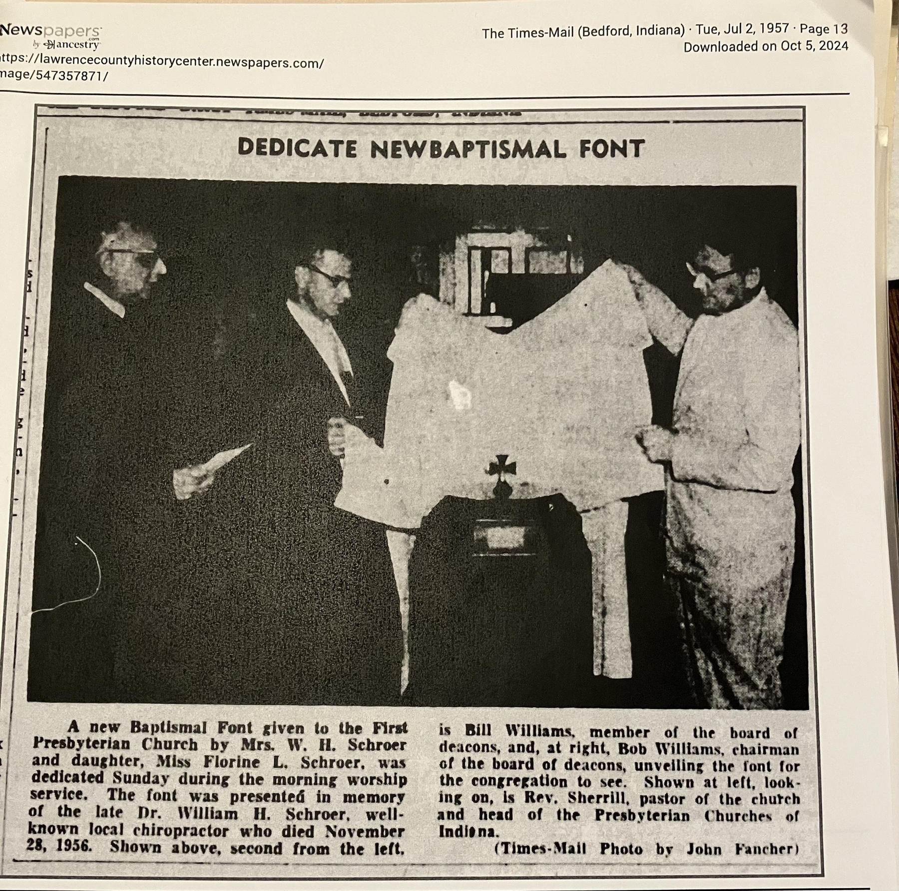 Auto-generated description: A group of men stands around a newly dedicated baptismal font, with one man holding a draped cloth covering it.