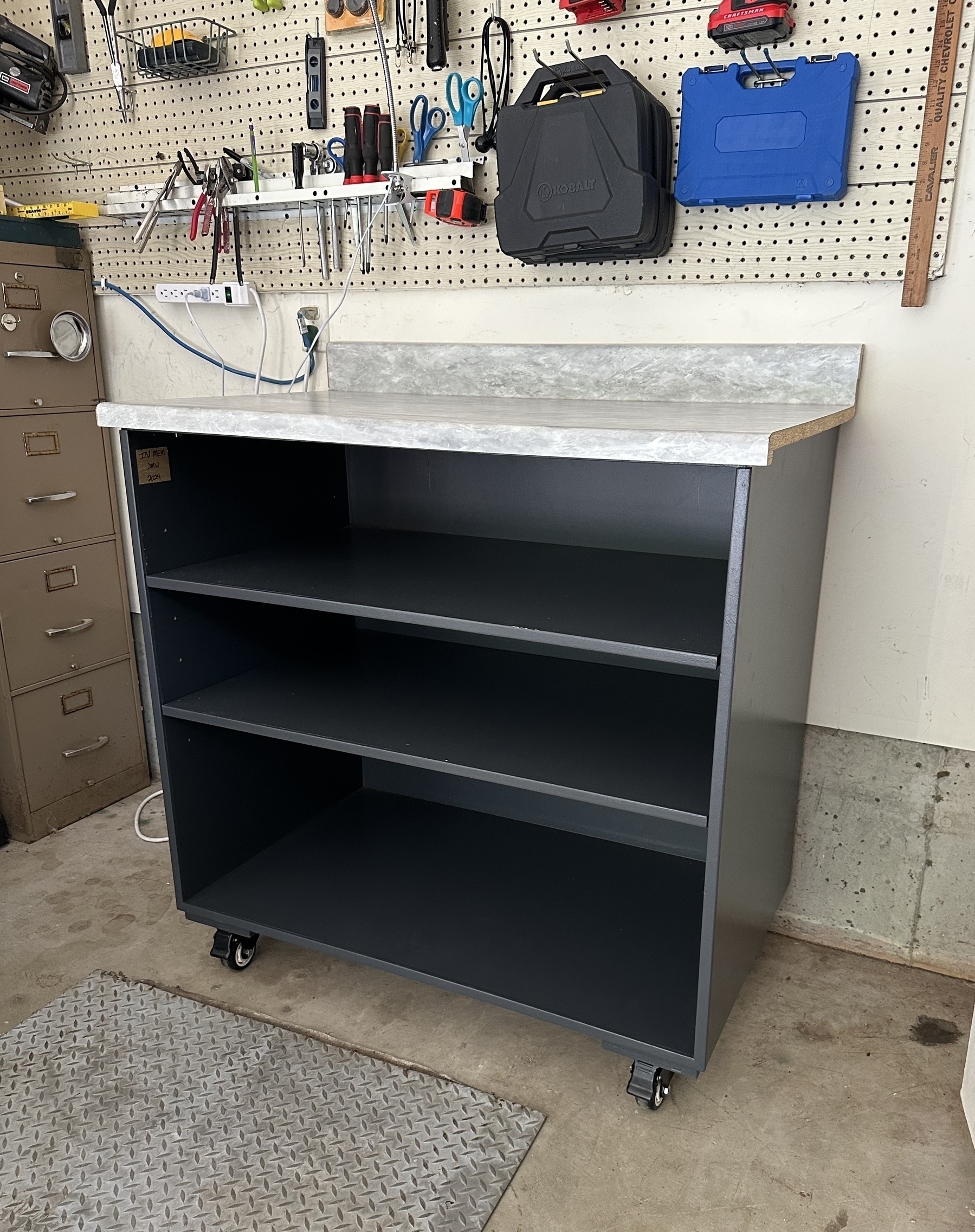 Auto-generated description: A workshop setup with a metal storage cabinet on wheels, a pegboard wall holding various tools, and a filing cabinet in the background.