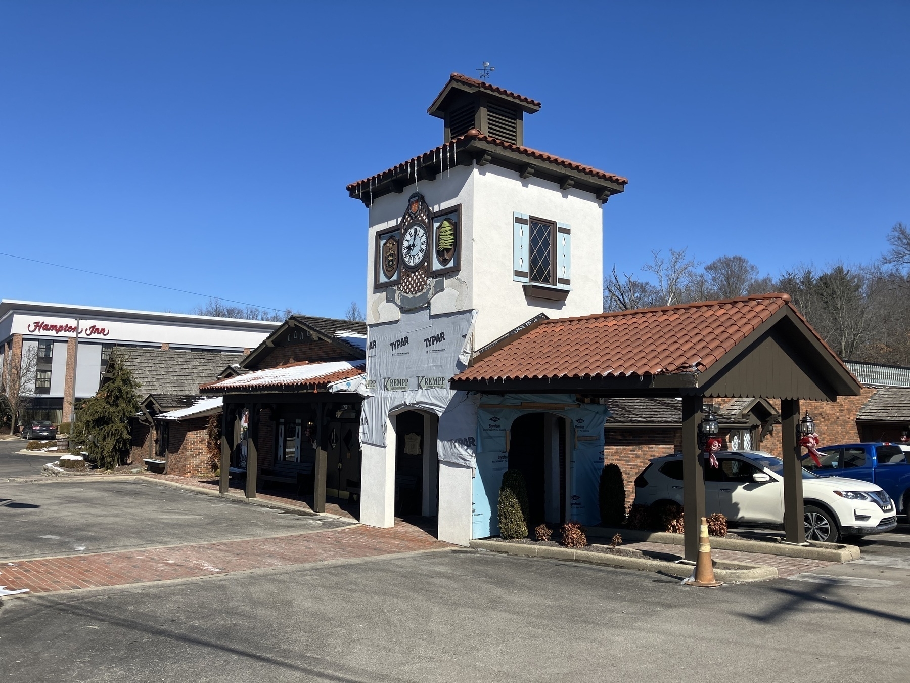 Auto-generated description: A charming building with a clock tower and red-tiled roof stands next to a Hampton Inn under a clear blue sky.