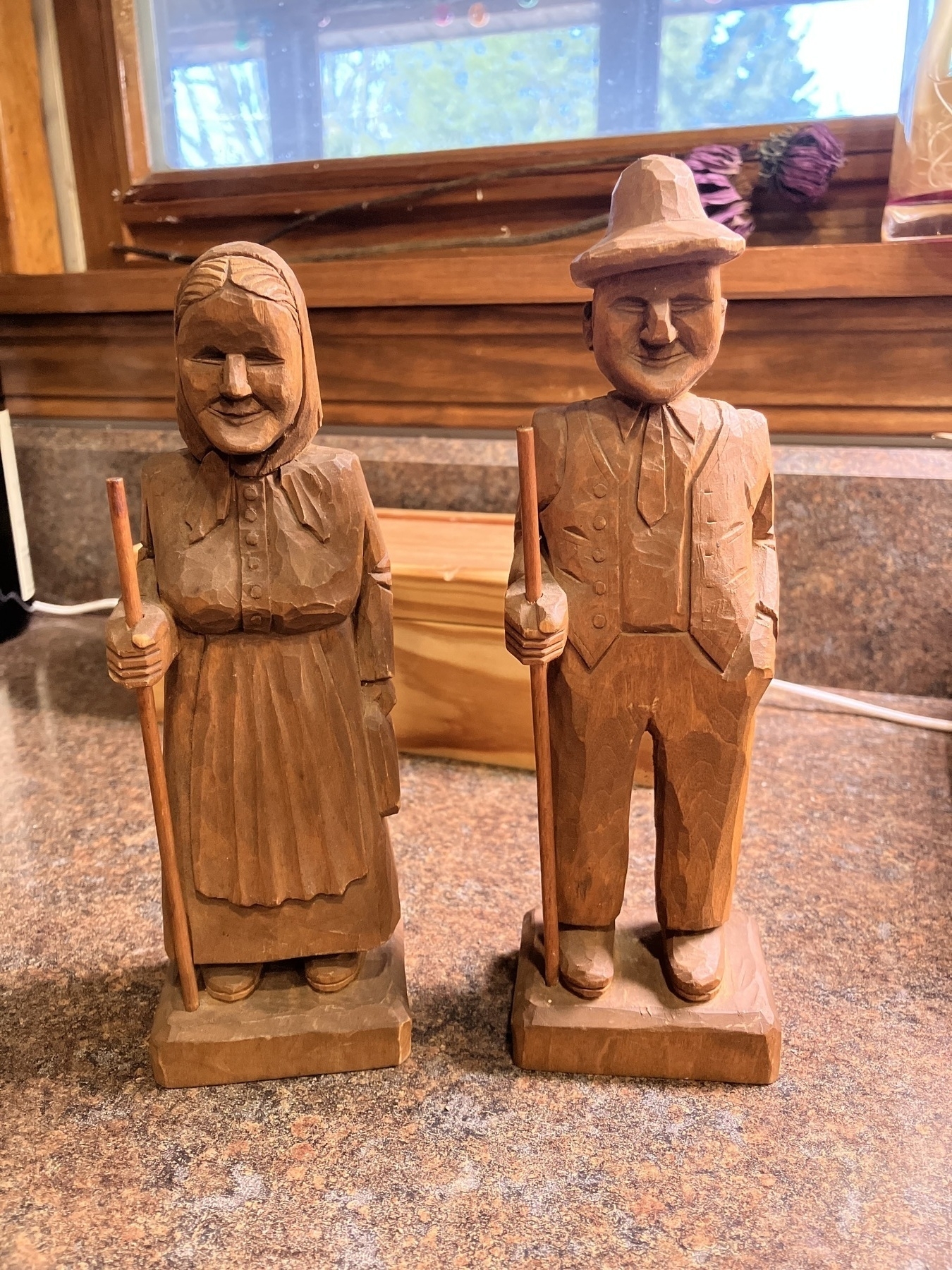 Auto-generated description: Two carved wooden figures of a woman and a man holding sticks are standing side by side on a countertop.