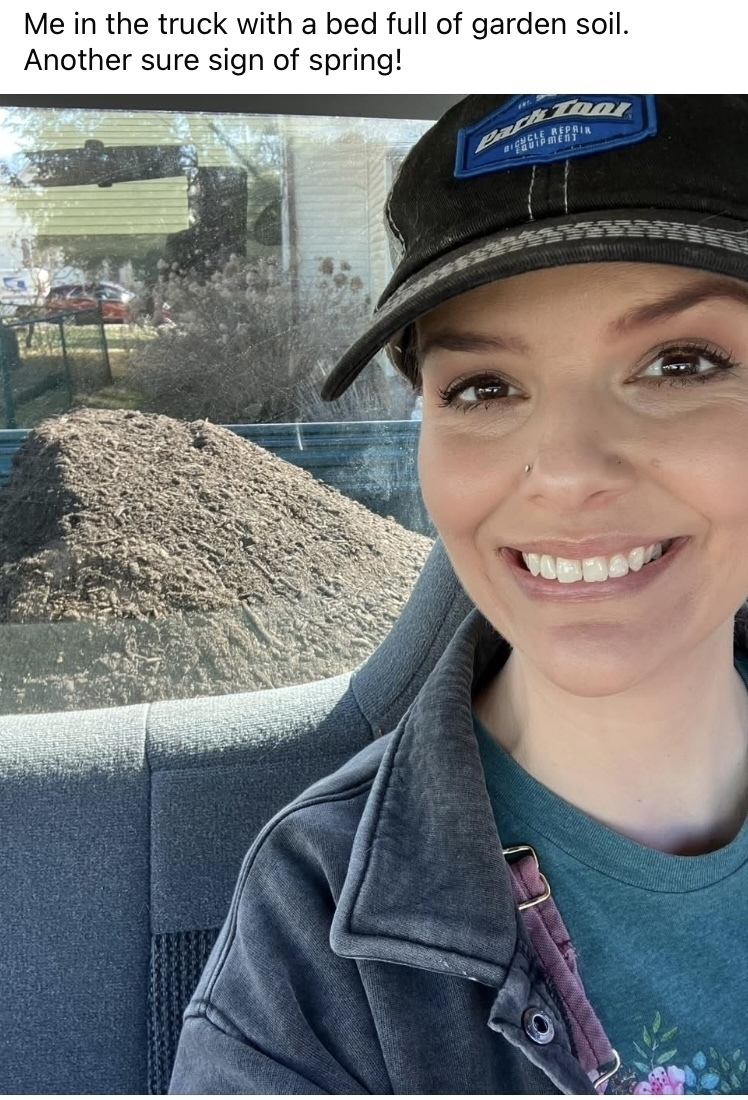 Auto-generated description: A person is smiling inside a truck with a pile of garden soil in the back seat, captioned as a sign of spring.