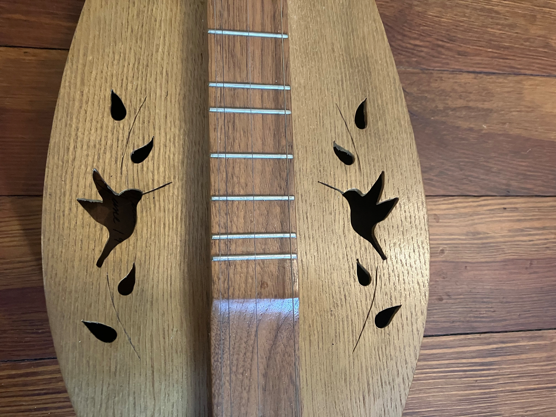 Auto-generated description: A stringed instrument with bird and leaf-shaped sound holes carved into its wooden body.