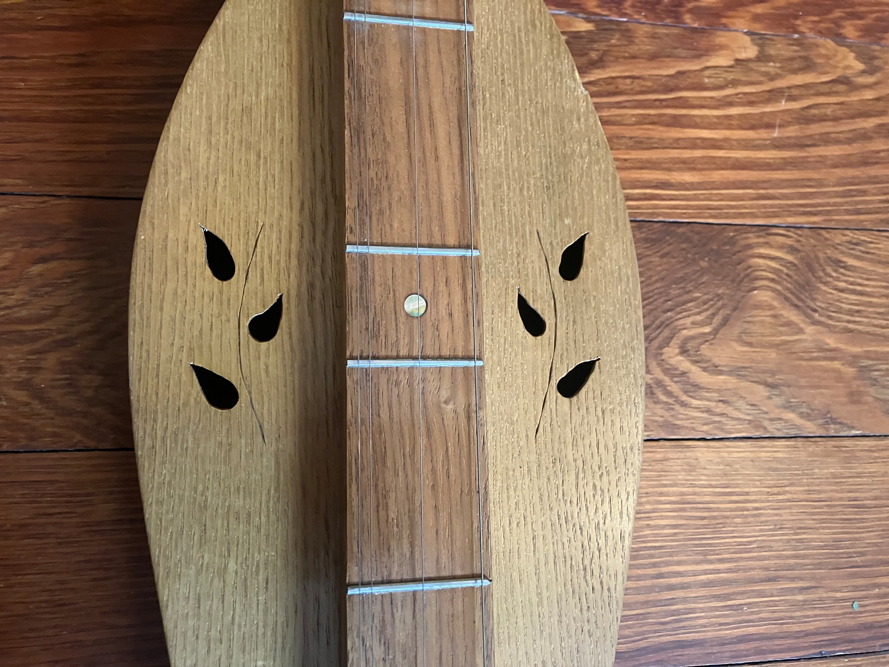 Auto-generated description: A wooden string instrument with leaf-shaped sound holes is placed on a wooden surface.