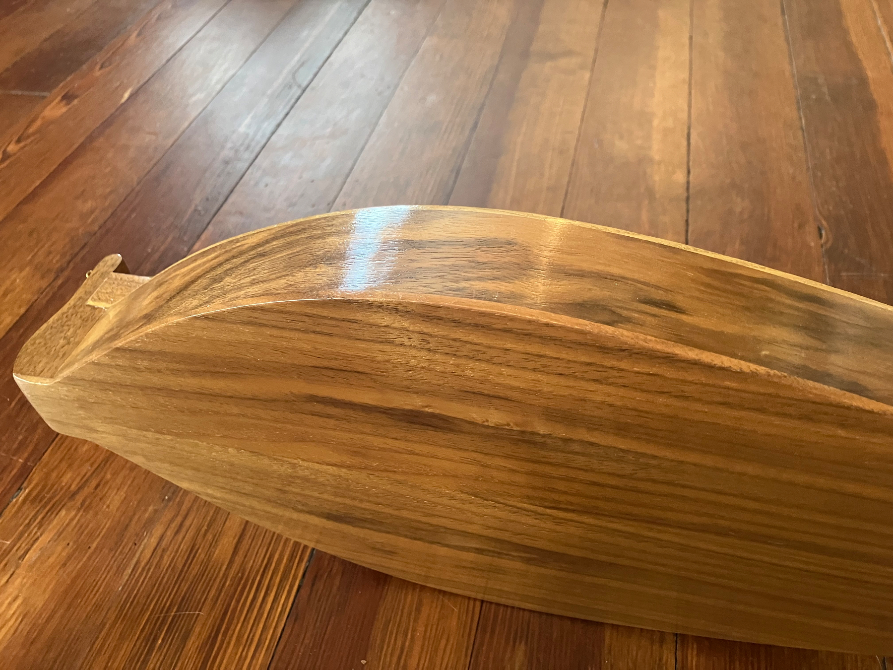 Auto-generated description: A wooden boat hull is resting on a polished wooden floor.