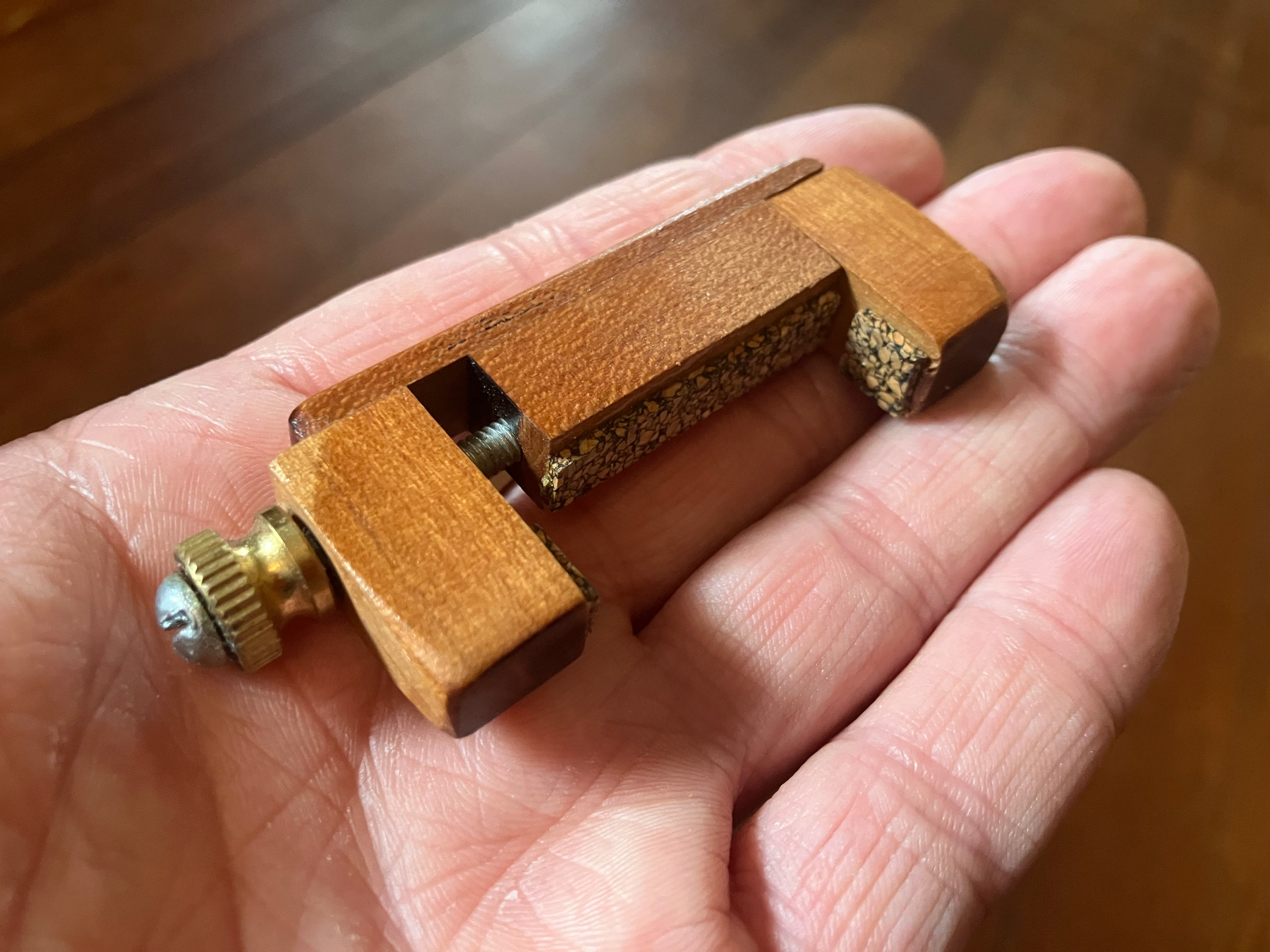 Auto-generated description: A small wooden clamp with a screw mechanism rests on an open palm.