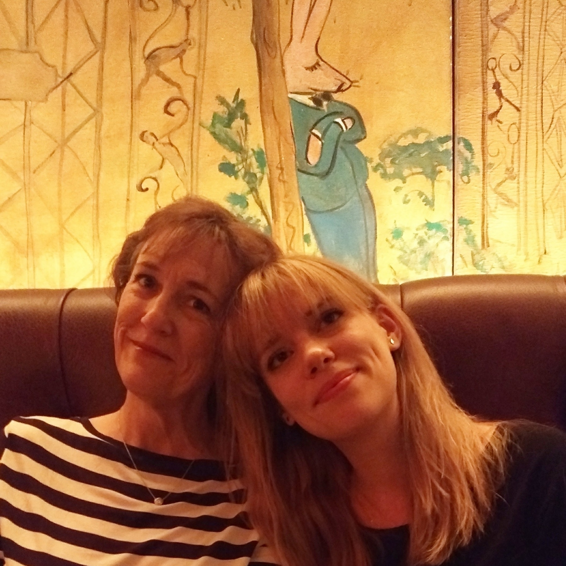 Mother and grown daughter with their heads together in a golden-glowed NY bar