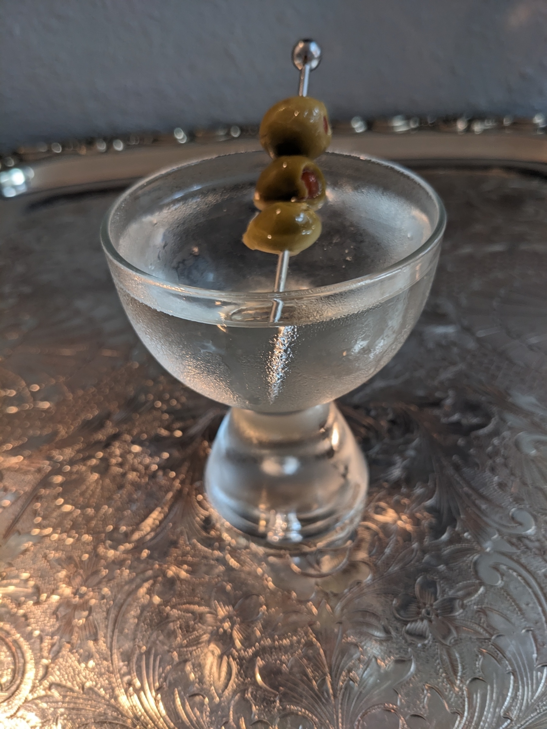 A Martini cocktail with three olives in a cold glass on a silver tray