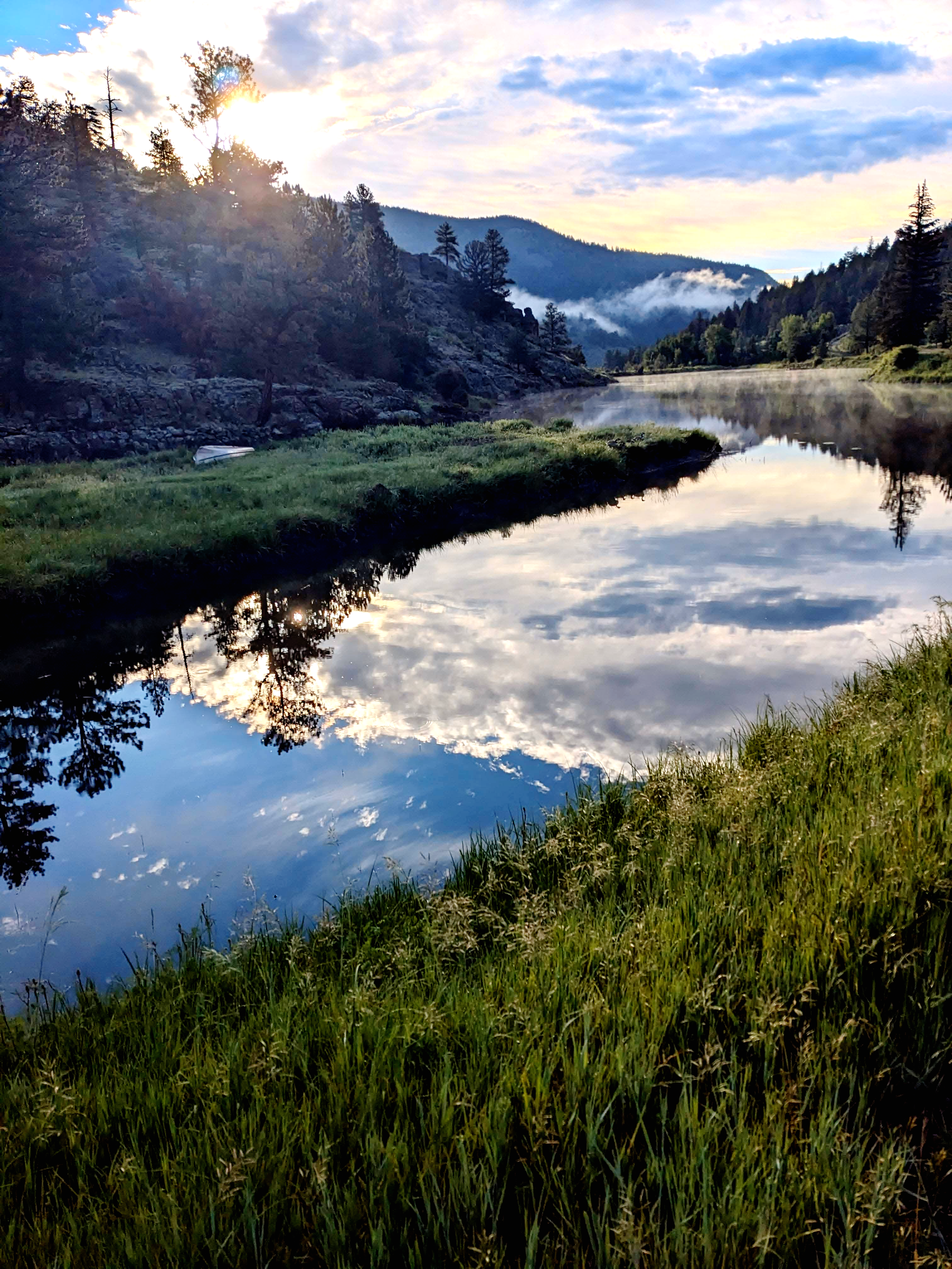 Clouds, trees, and mountains reflected in a Rocky Mountain lake at dawn.