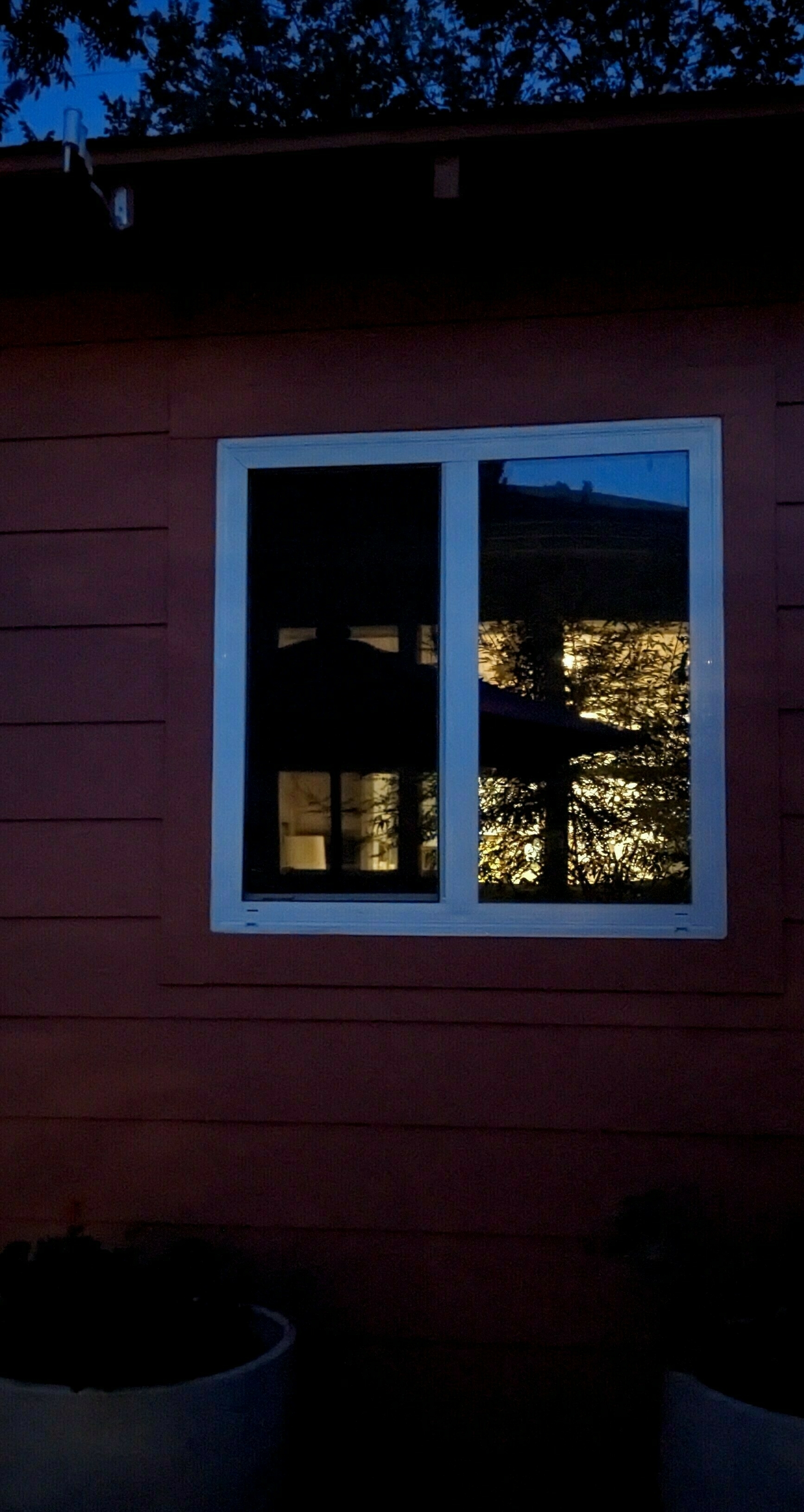 Auto-generated description: A window reflects warm interior lights and a silhouetted tree, set against a dusky backdrop.