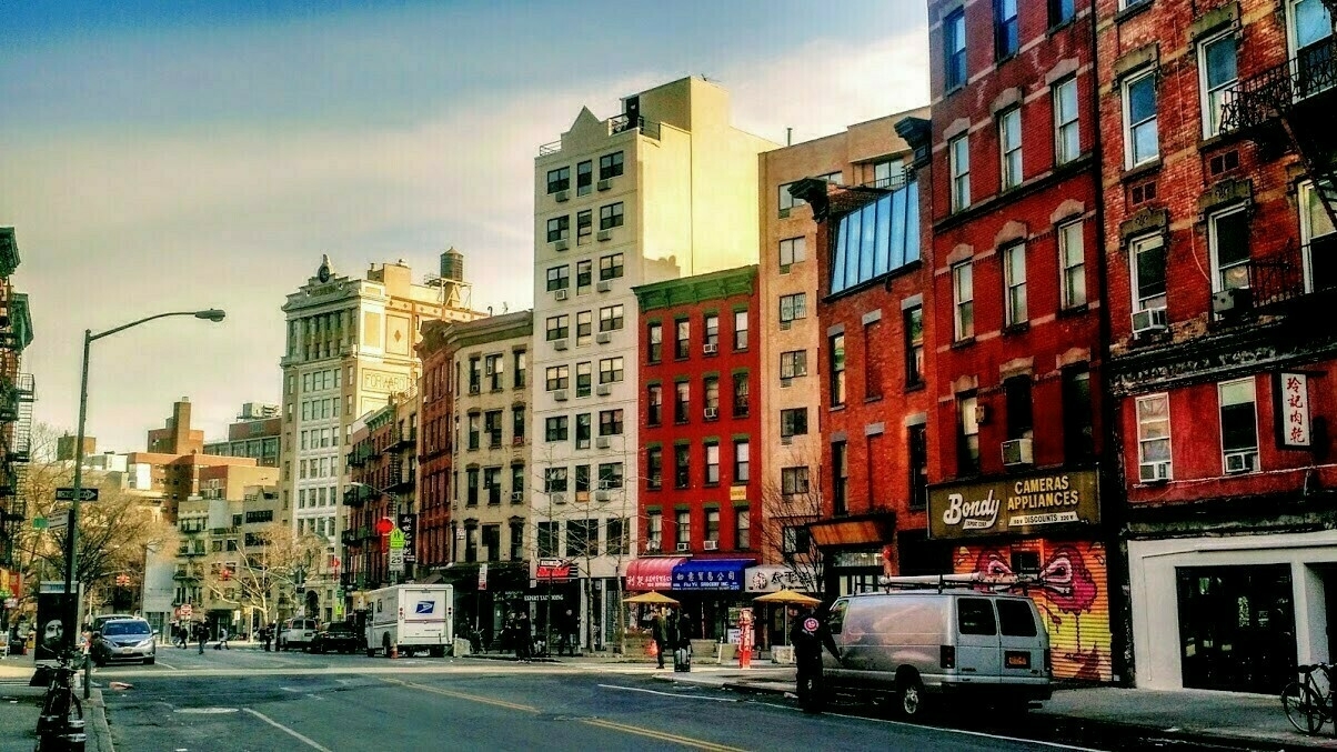 Looking down a street bordered by a row of red and cream-colored brick buildings from the 19th and 20th centuries.