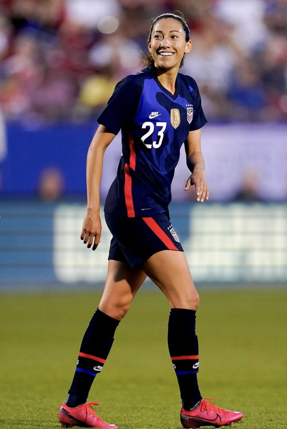 U.S. women's soccer player Christian Press wearing a navy blue uniform with the number 23 is on the field smiling.