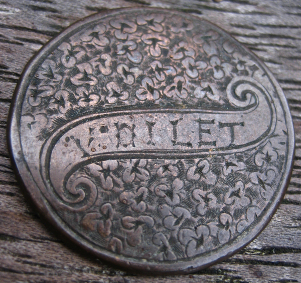 A round metal coin with ornate floral engravings and the word VOILET displayed prominently.