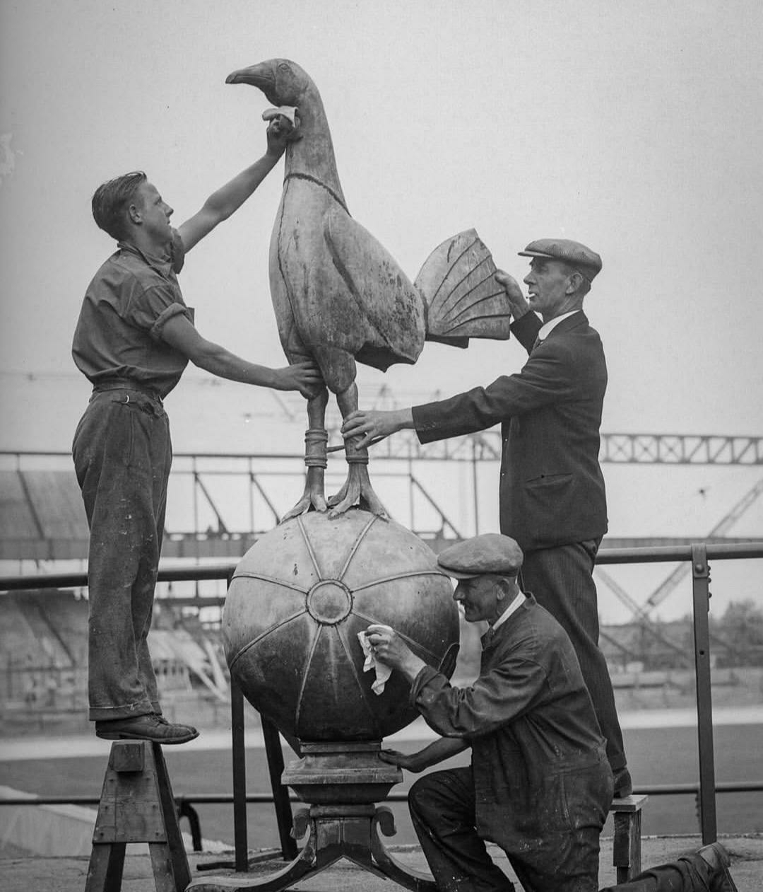 Auto-generated description: Three men are cleaning and polishing a large bird statue perched on a ball.