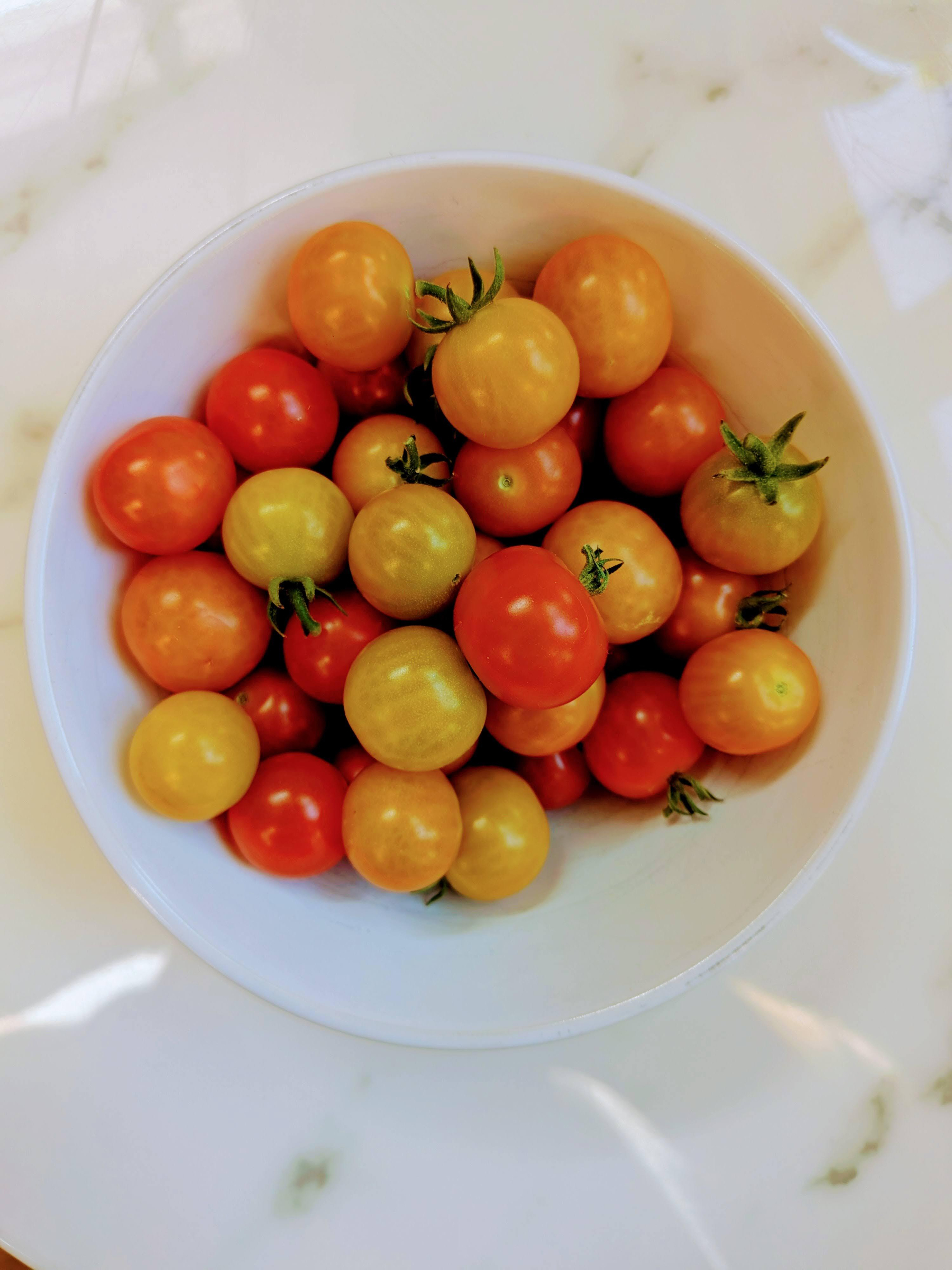 Auto-generated description: A white bowl filled with small, red and yellow cherry tomatoes sits on a marble surface.