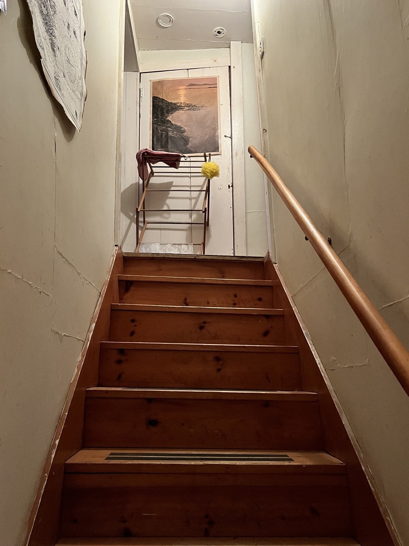 Looking up a steep staircase with wooden clothes drying rack at the top. Wooden handrail on the right. 