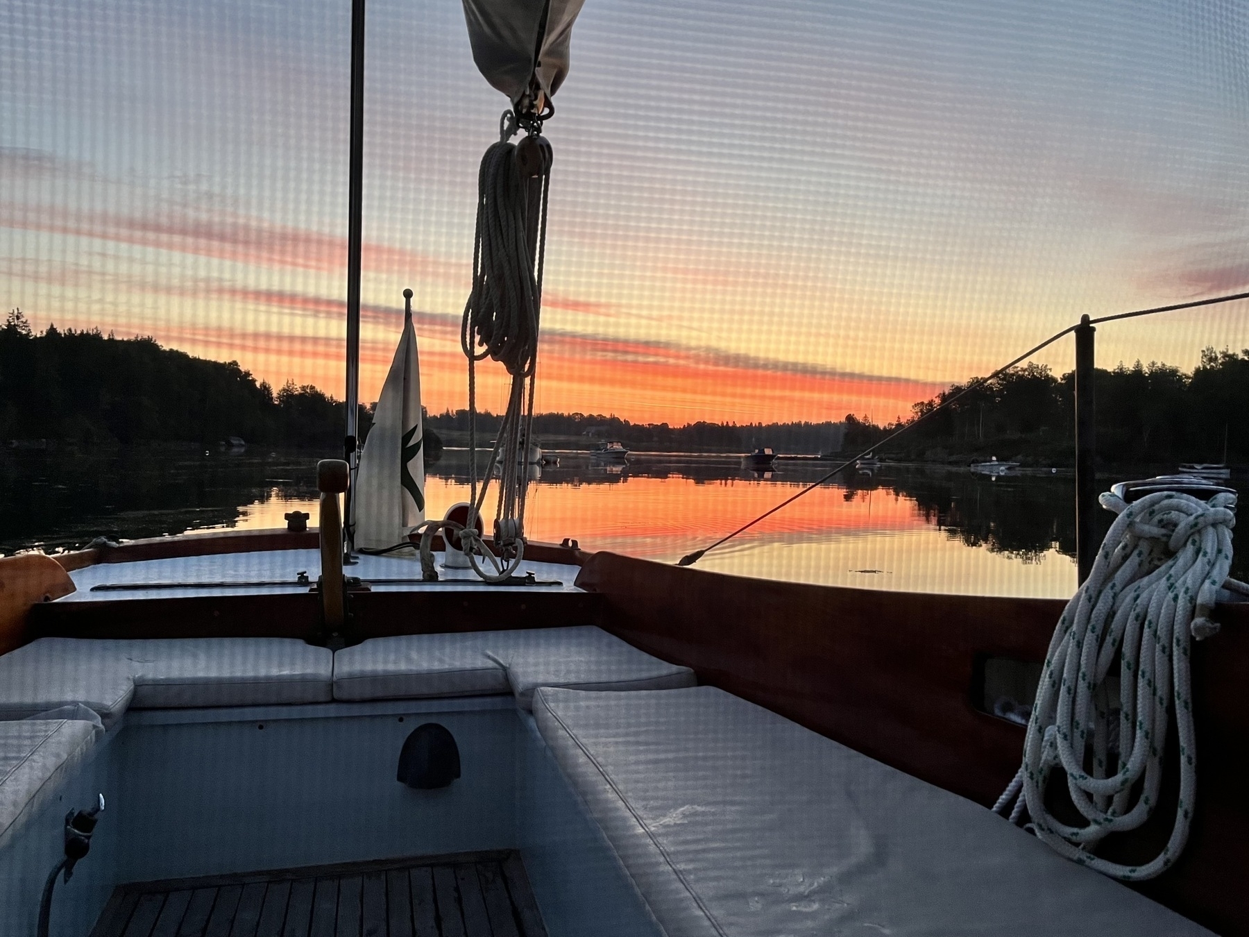 Glowing orange clouds reflected in water astern of sailboat