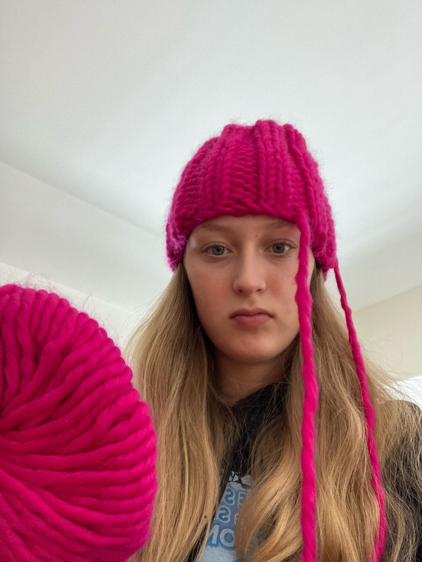 Partially knit pink hat on head with ball of yarn in foreground left corner