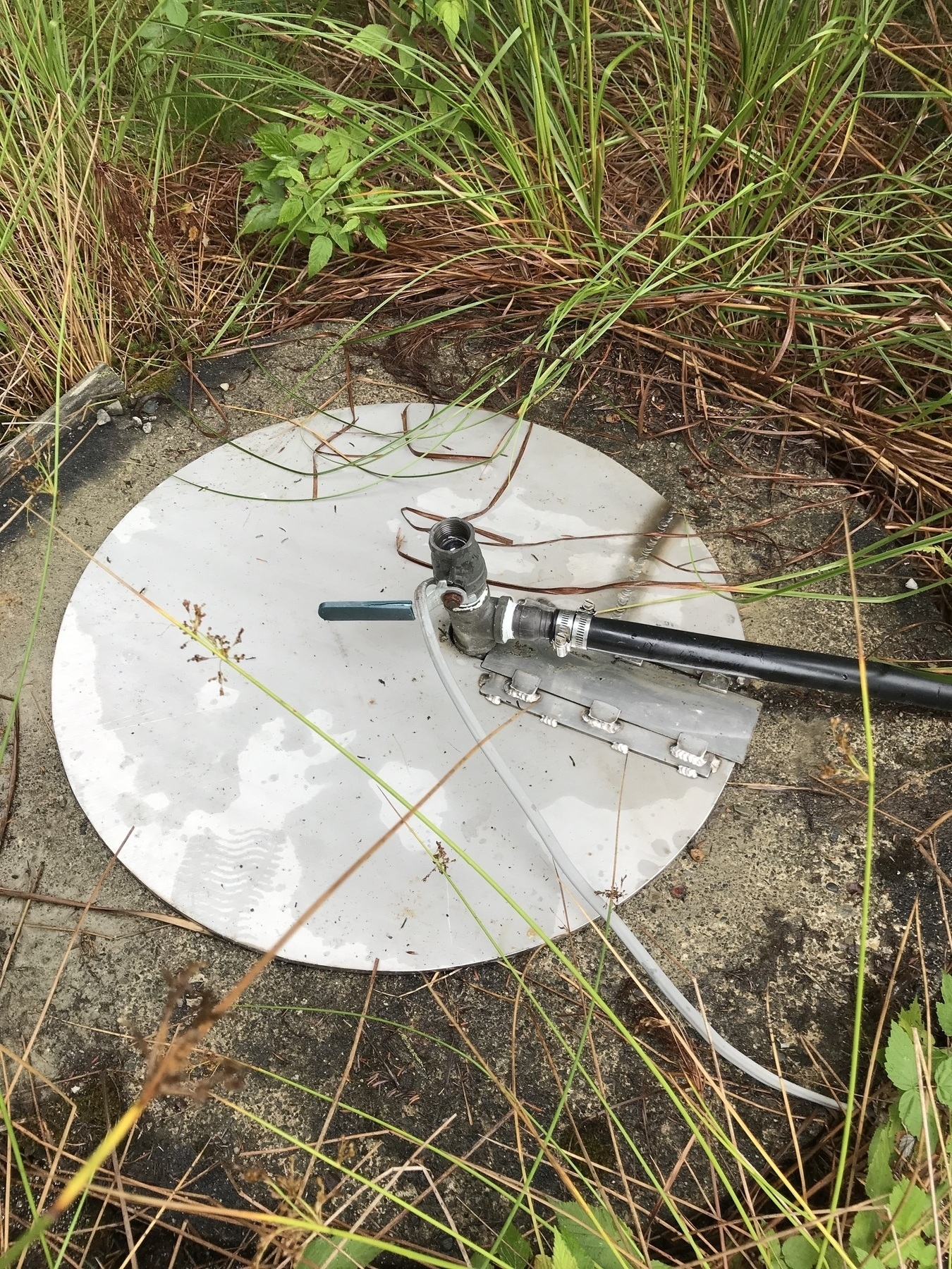Circular metal cover on concrete well with water hose coming through the center. 